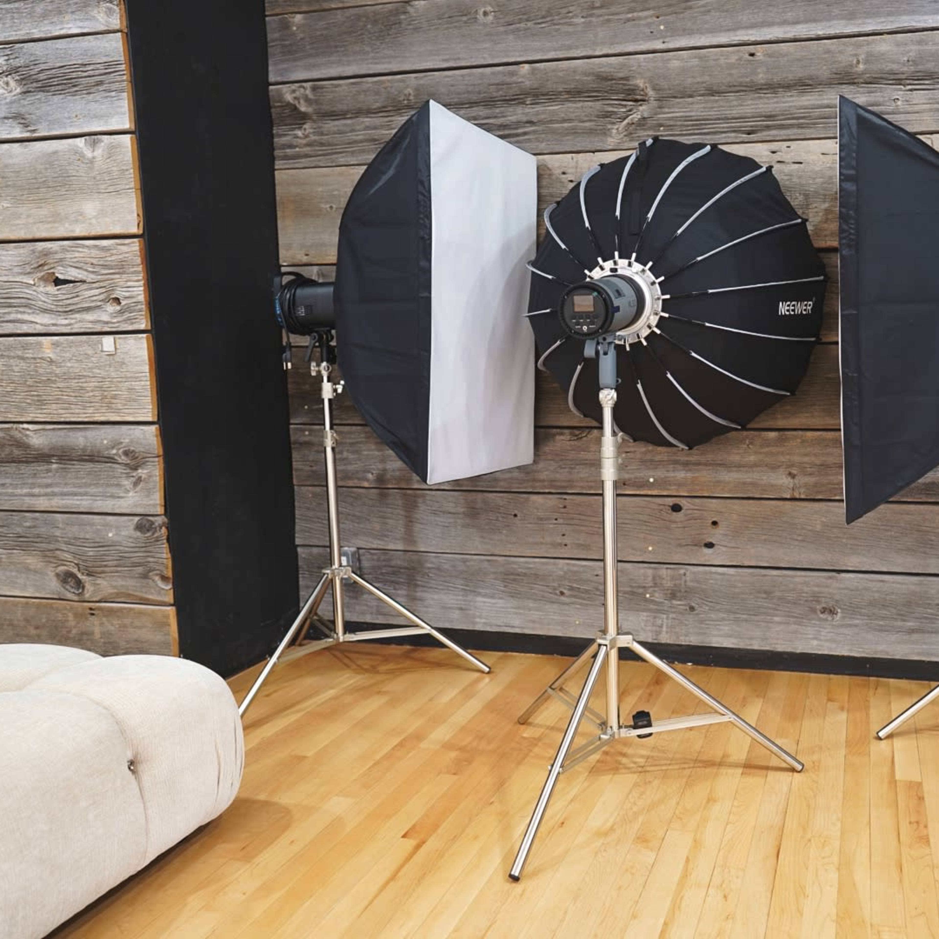Three photography light setups on stands positioned in front of a wooden wall.