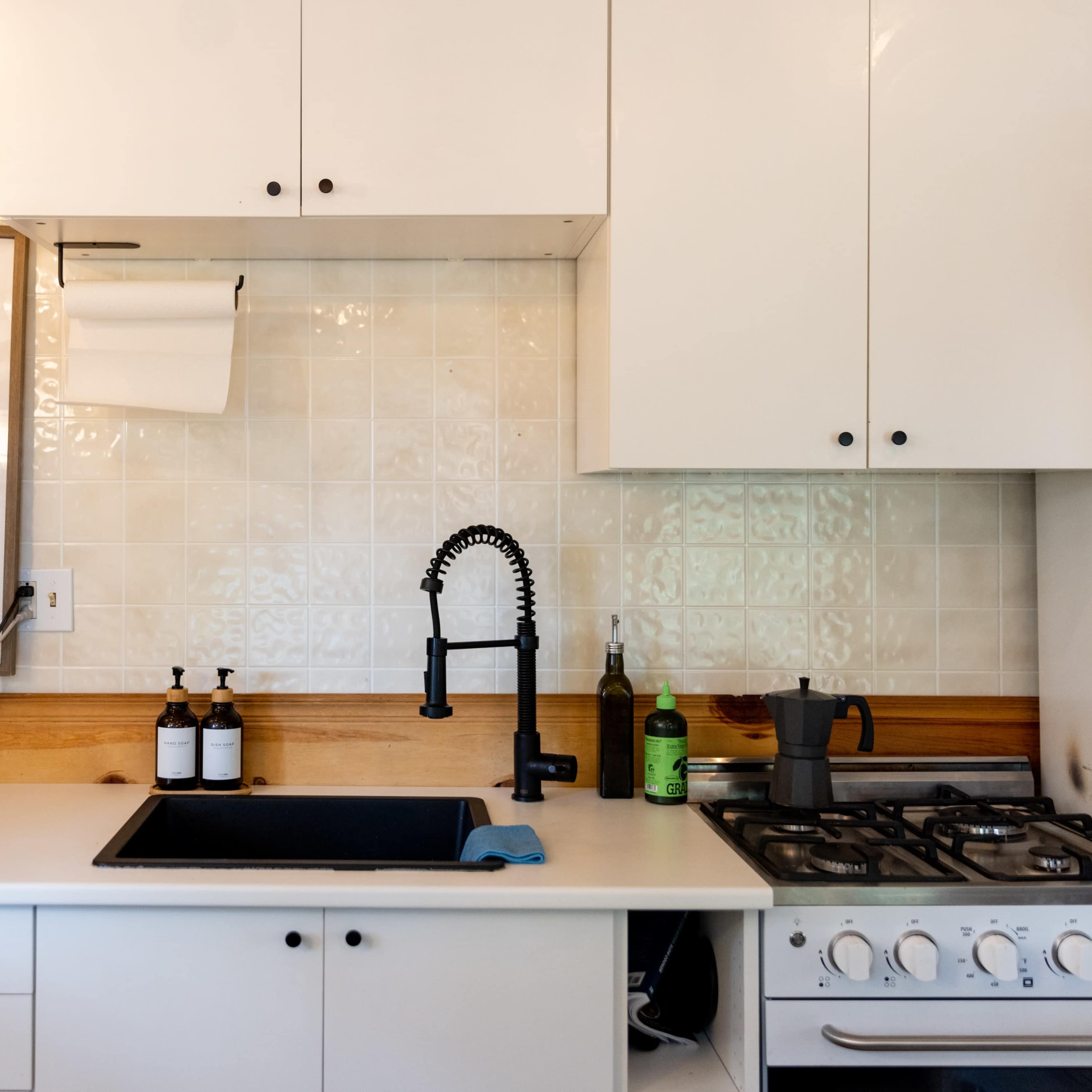 A modern kitchen features white cabinets, a black faucet above a stainless steel sink, a coffee maker, and a gas stove on a wooden countertop.