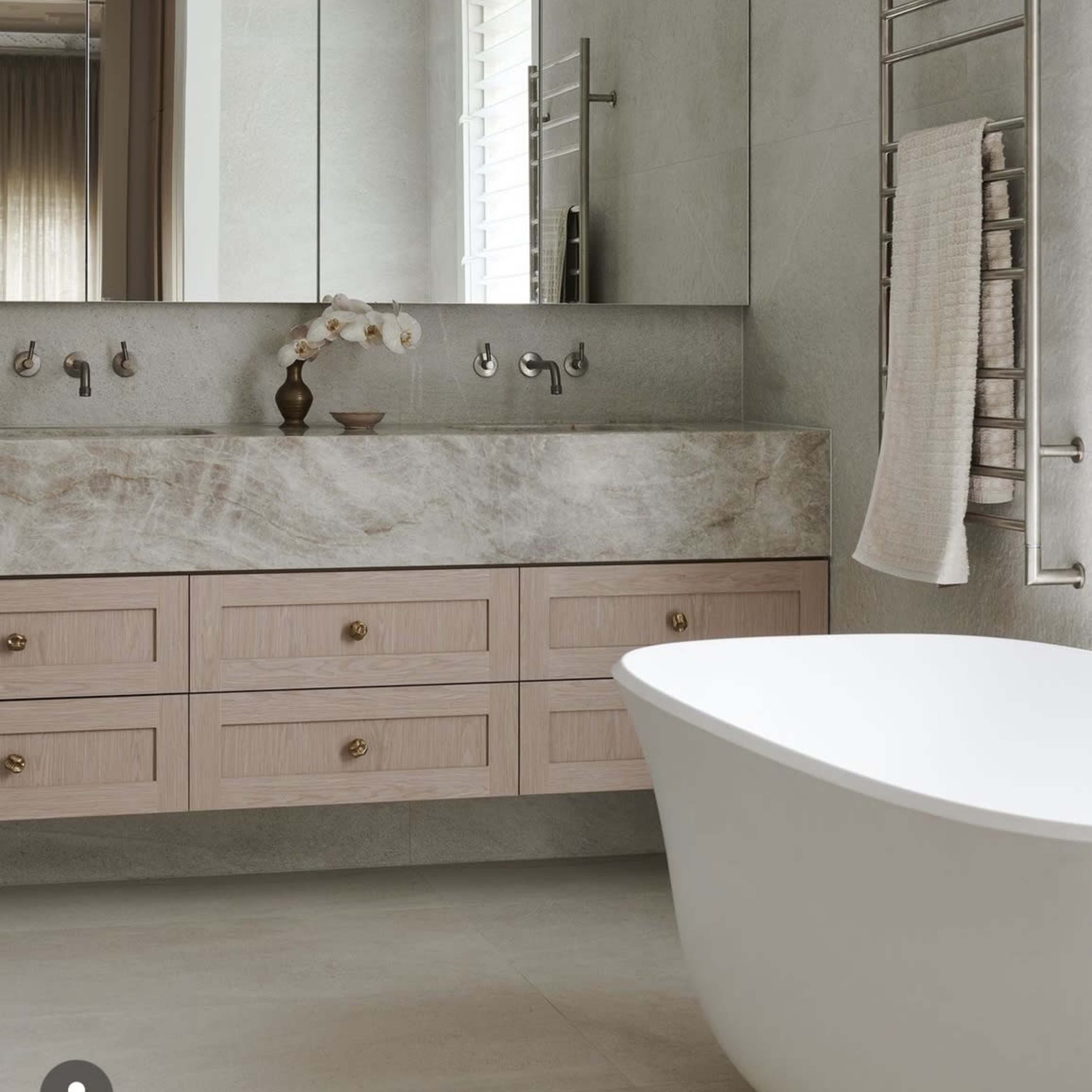 A modern bathroom featuring a freestanding white bathtub, a countertop with a sink and wooden cabinetry, and large mirrors reflecting the space.