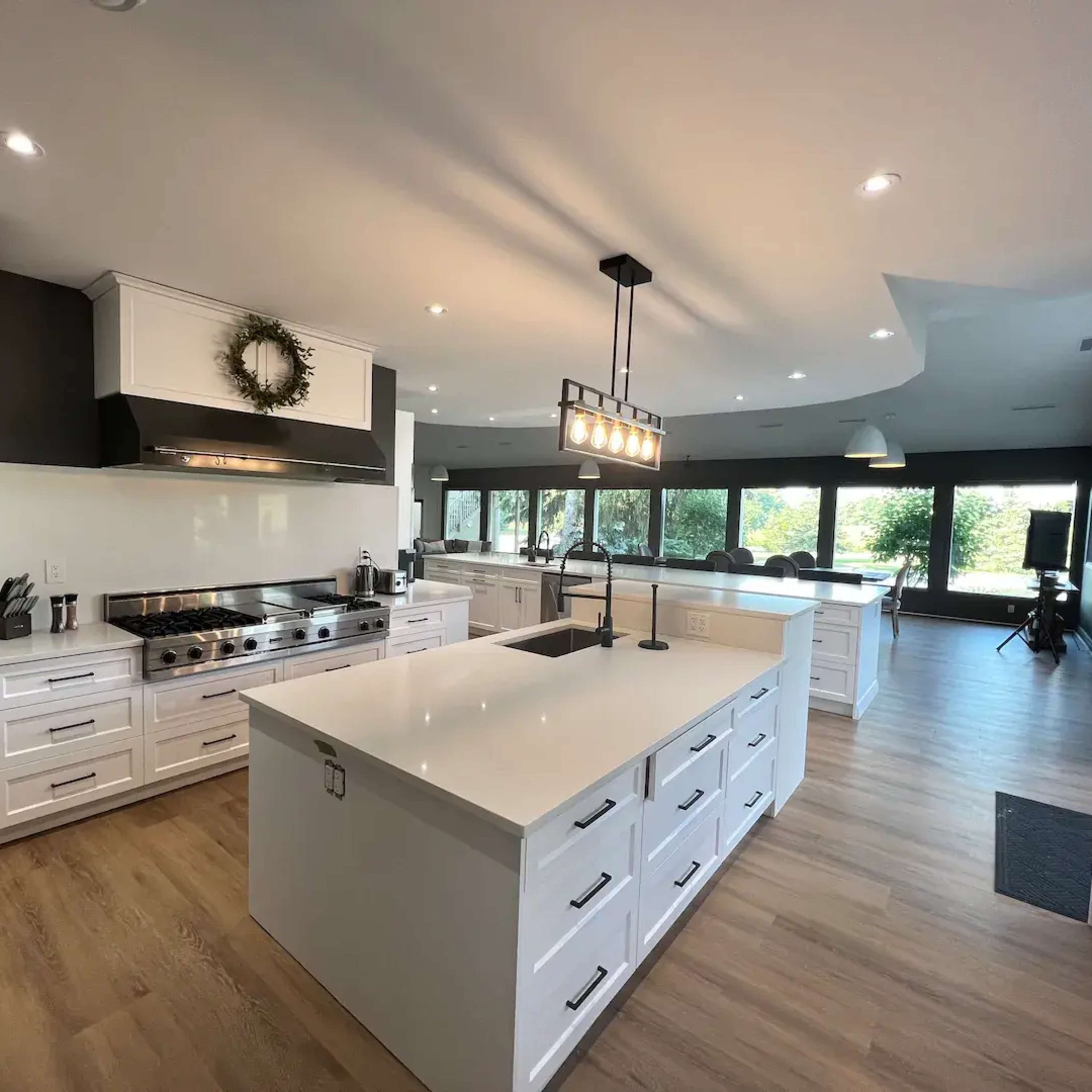 The kitchen features modern white cabinetry, a large island with a quartz countertop, and stainless steel appliances, all set against a backdrop of large windows.