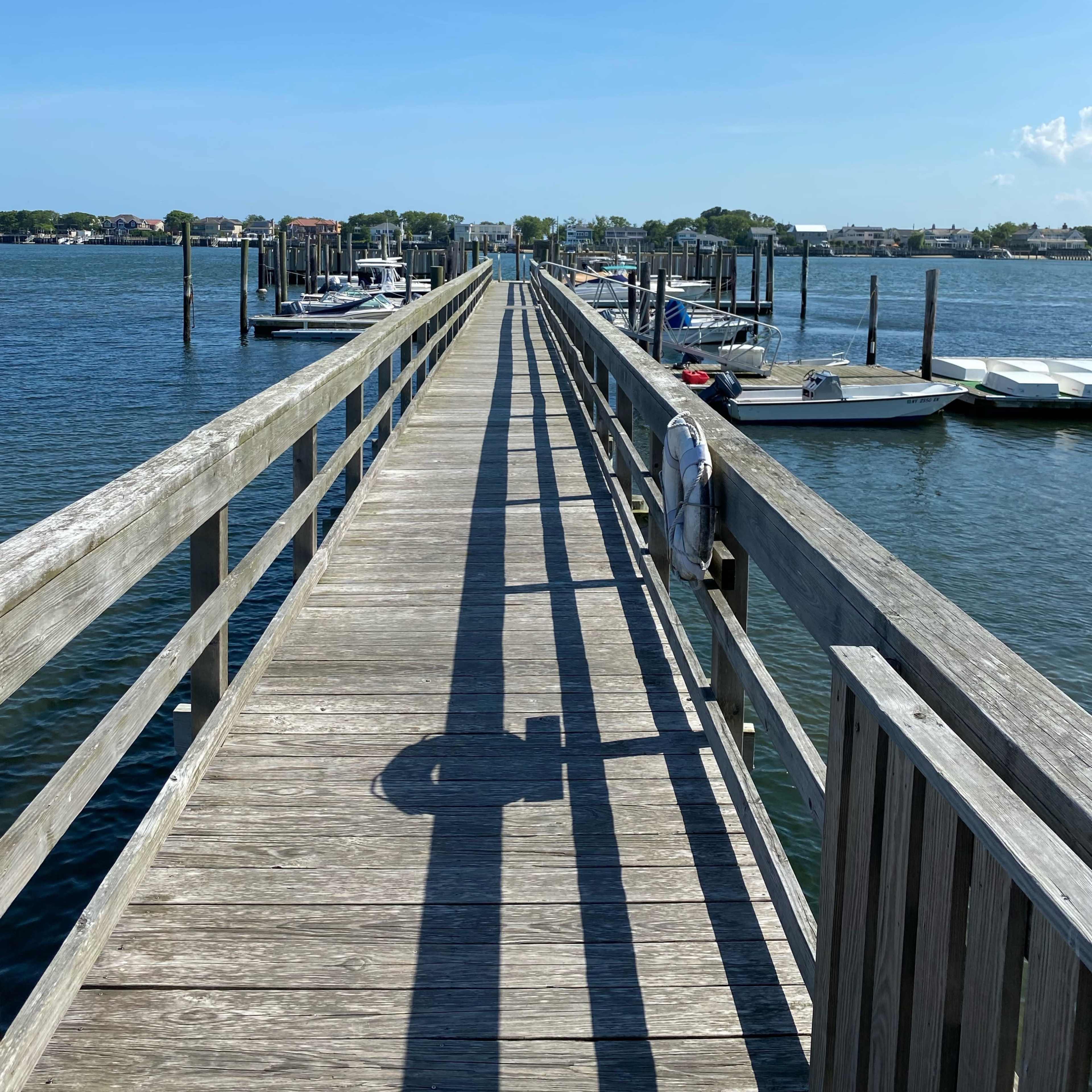 A wooden dock extends over the water, lined with boats on either side under a clear blue sky.