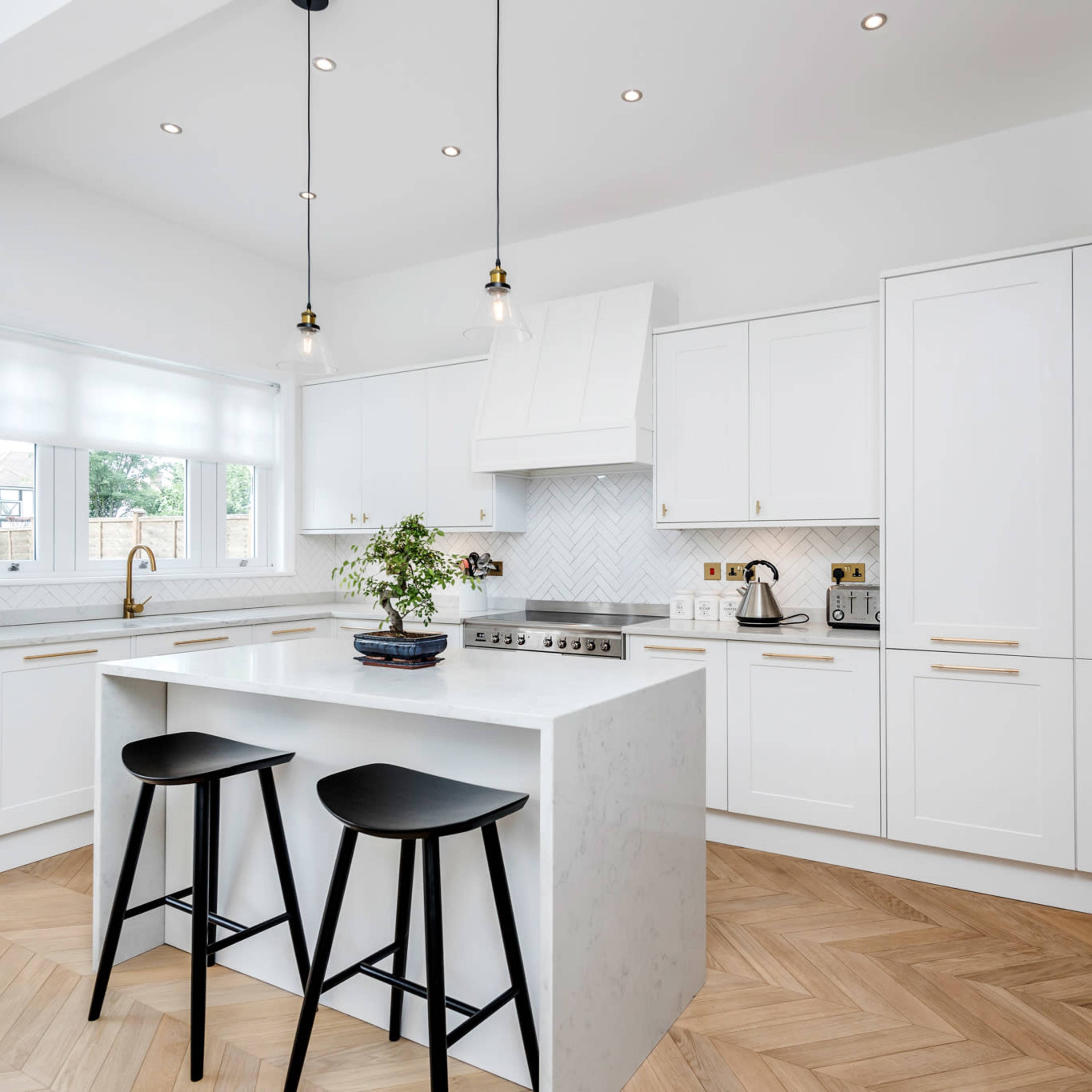 A modern kitchen with white cabinetry, a large island with two black stools, and herringbone-patterned flooring.