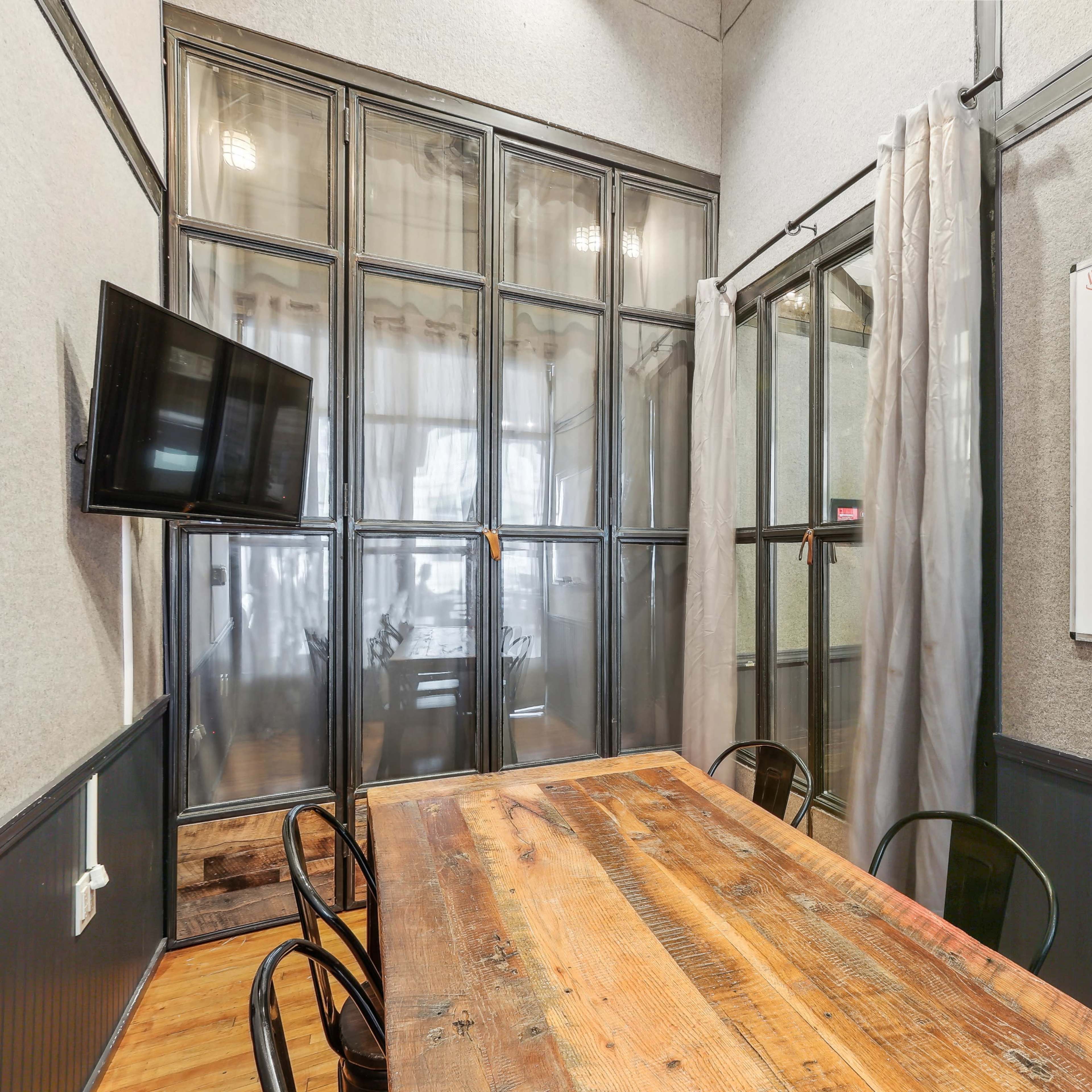 A conference room with a wooden table, black chairs, a wall-mounted TV, and a whiteboard.