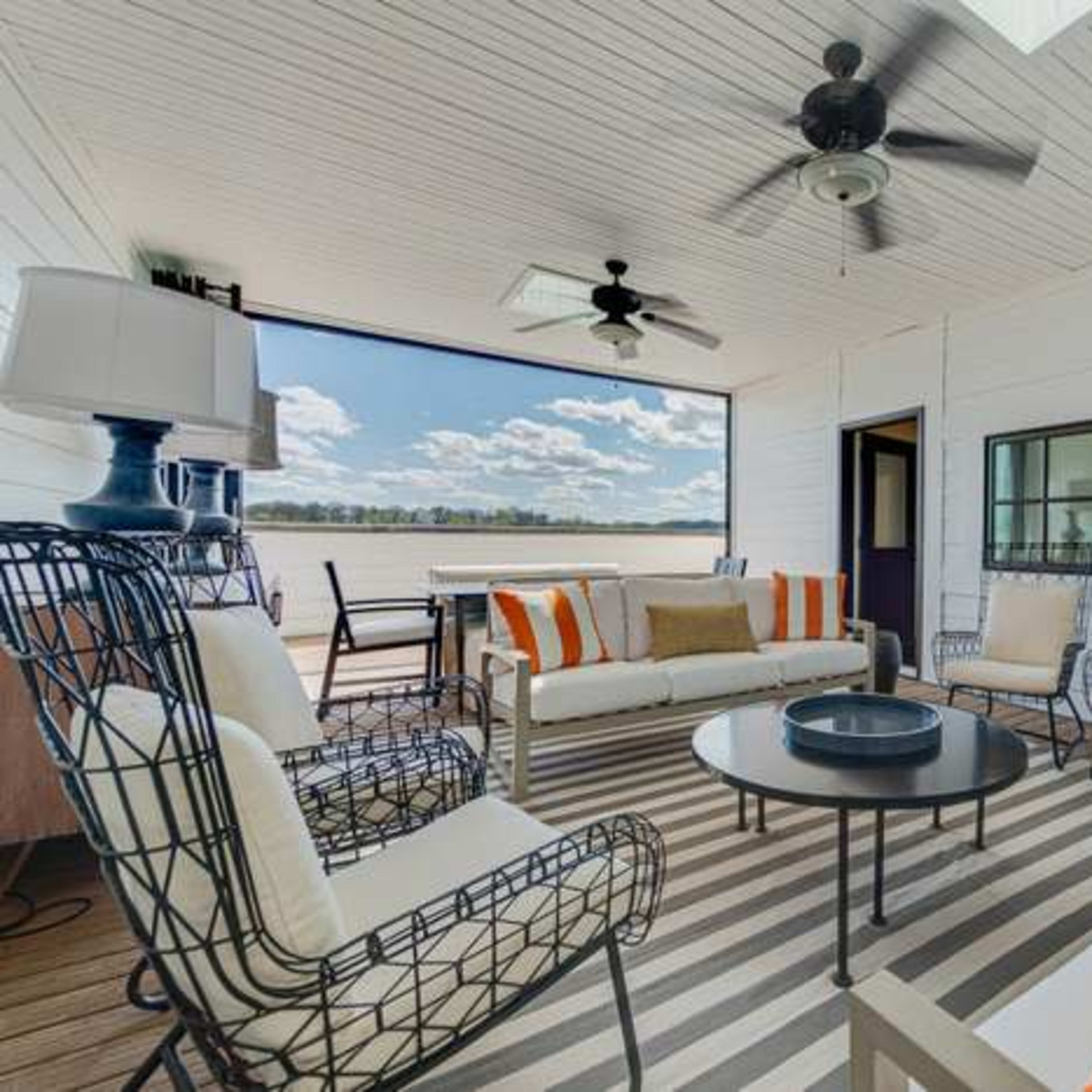 A covered outdoor seating area with metal framed chairs and sofa, a round table, and a light fixture, all arranged on a striped rug.