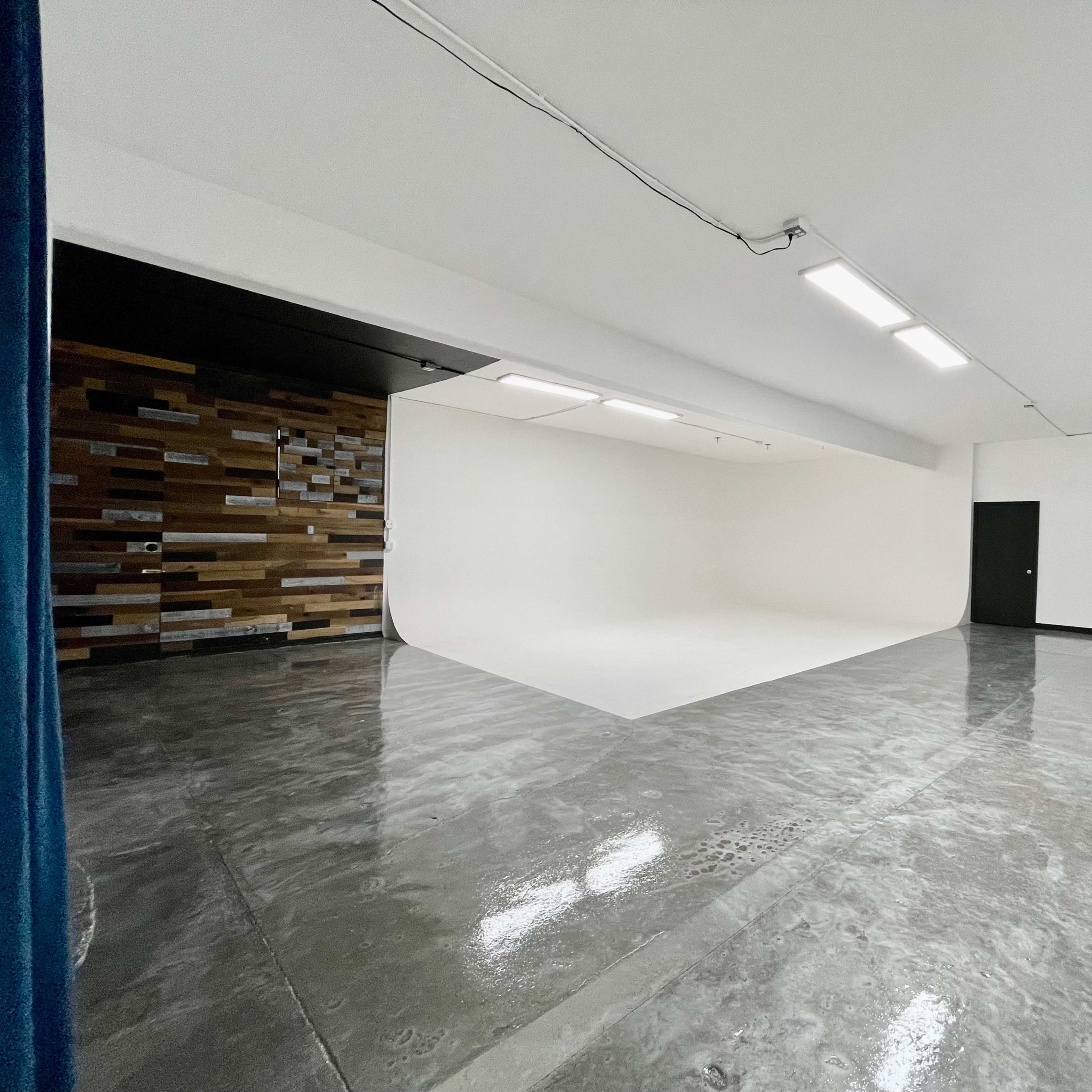 A minimalist studio space with a curved white backdrop and a polished concrete floor.