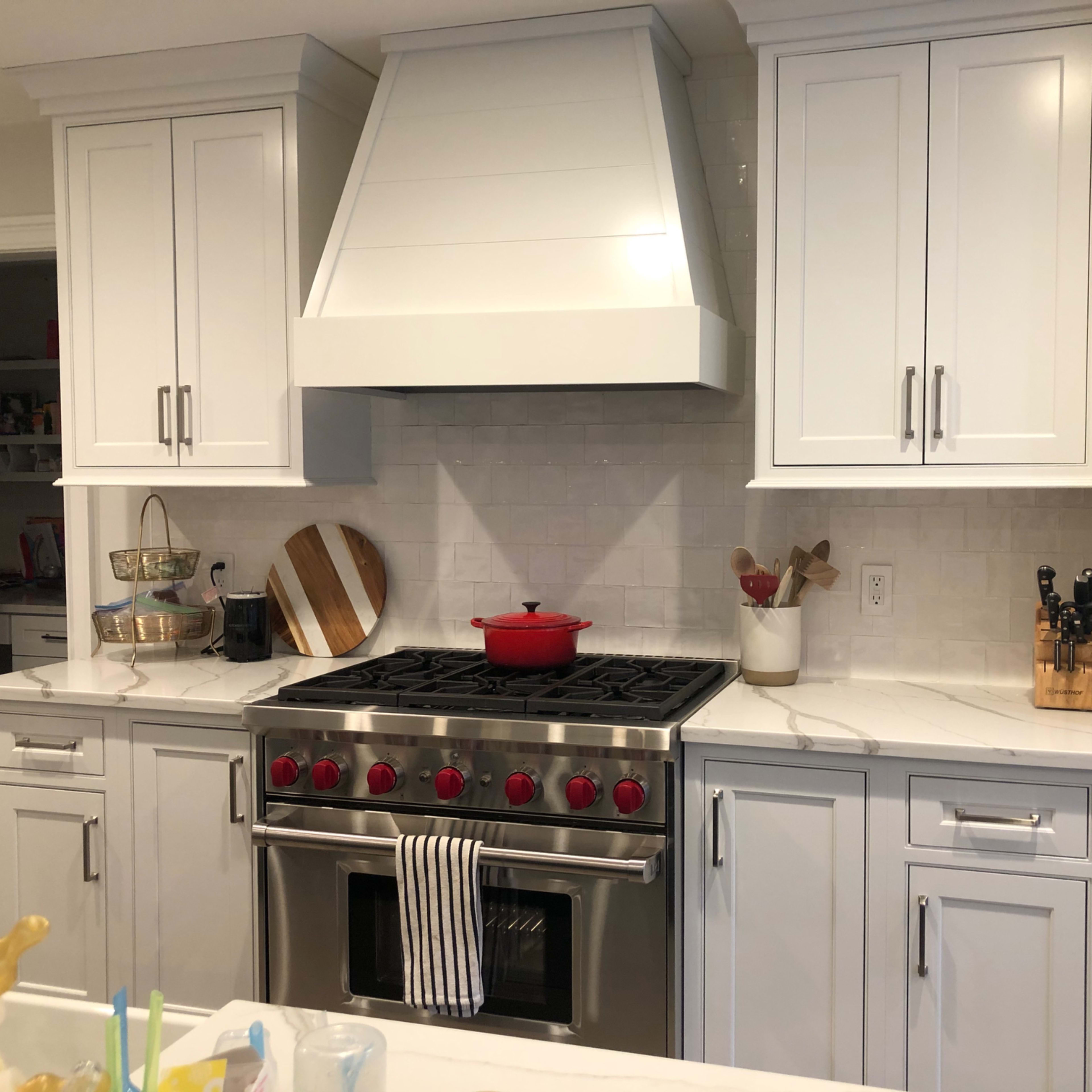 A modern kitchen featuring white cabinetry, a large stainless steel oven range, a red pot on the stove, and a marble countertop.