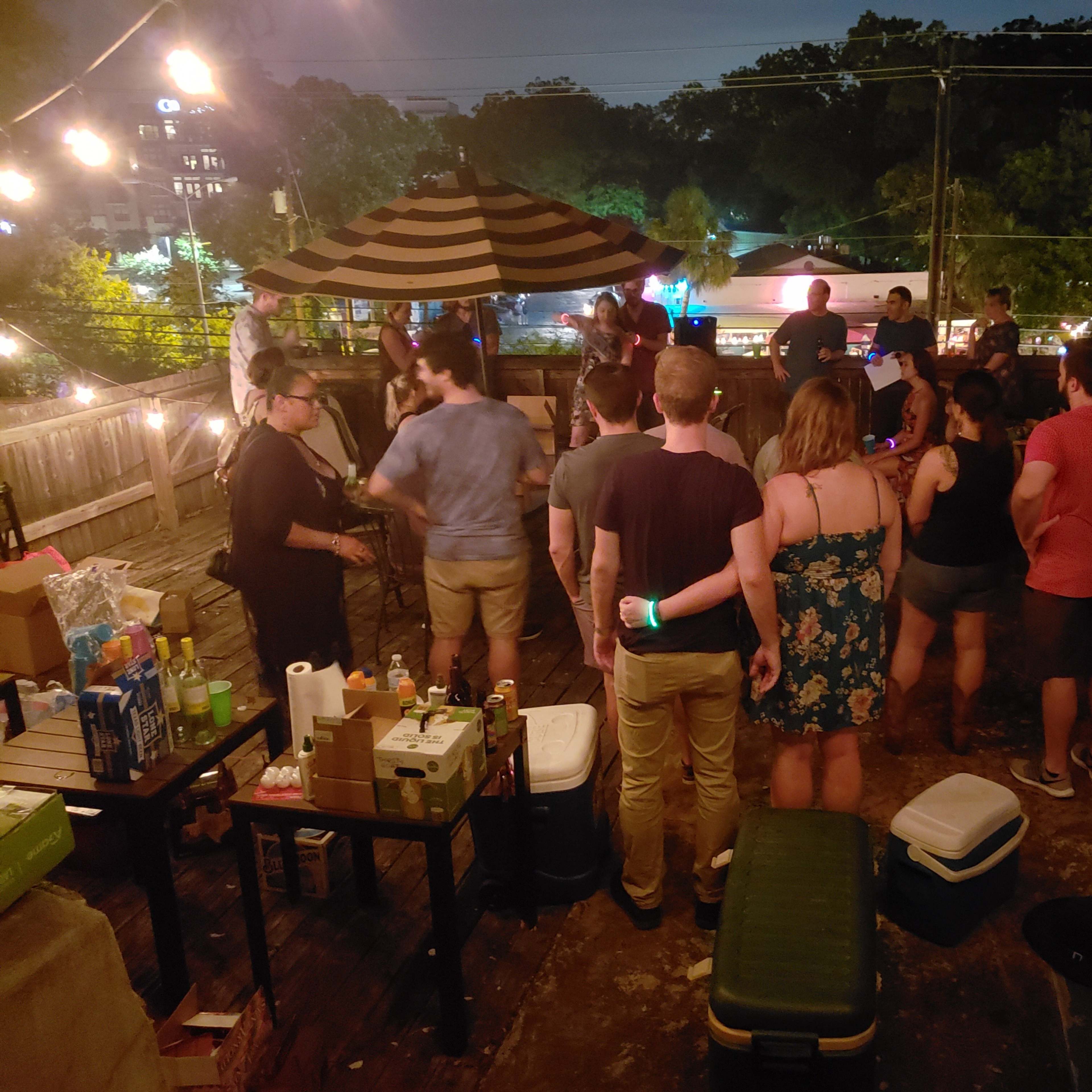 A group of people socialize on a rooftop adorned with string lights, while food and drinks are arranged on tables.