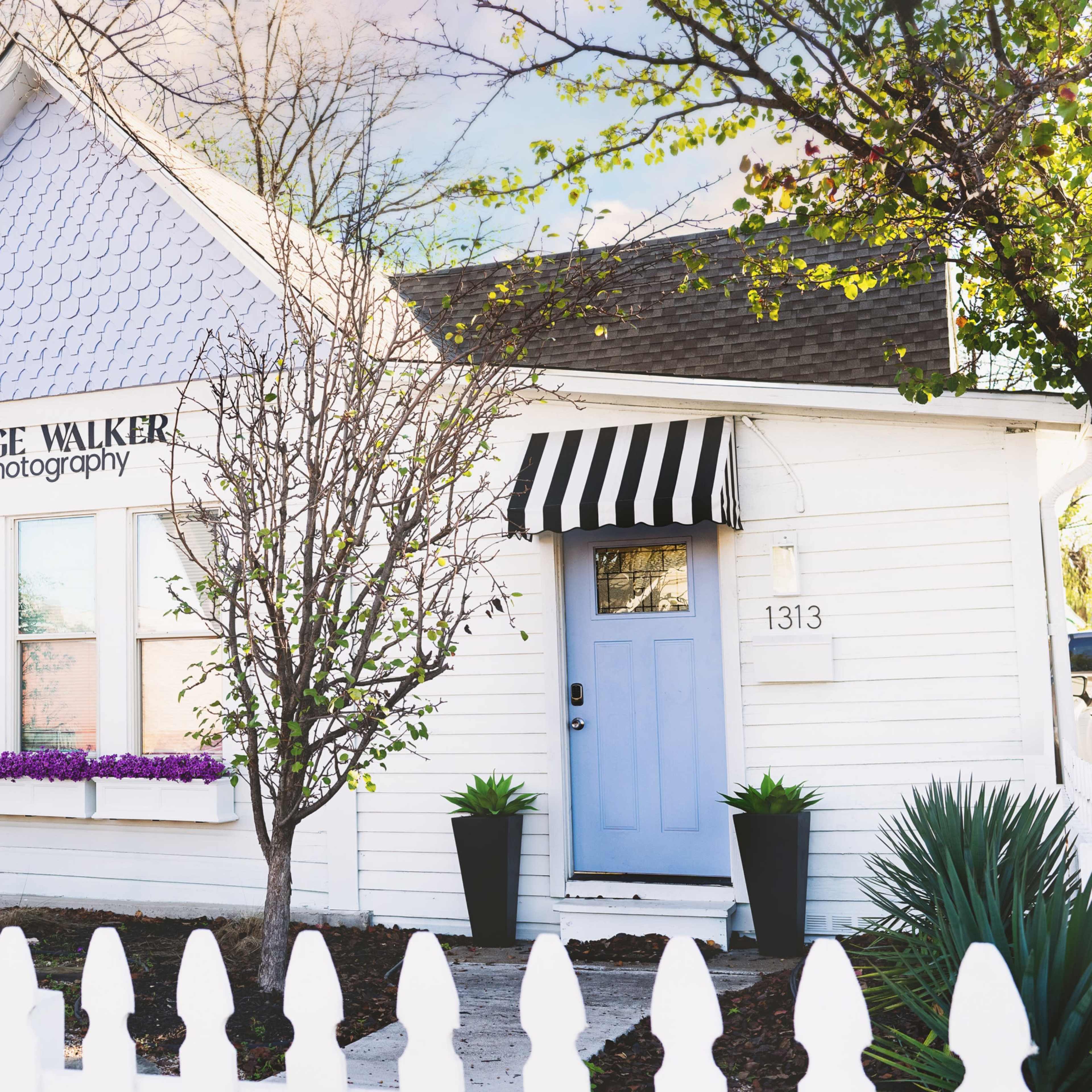 A white cottage with lavender accents and a striped awning houses Paige Walker Photography, alongside a separate space for Ashley McNairb Artistry.
