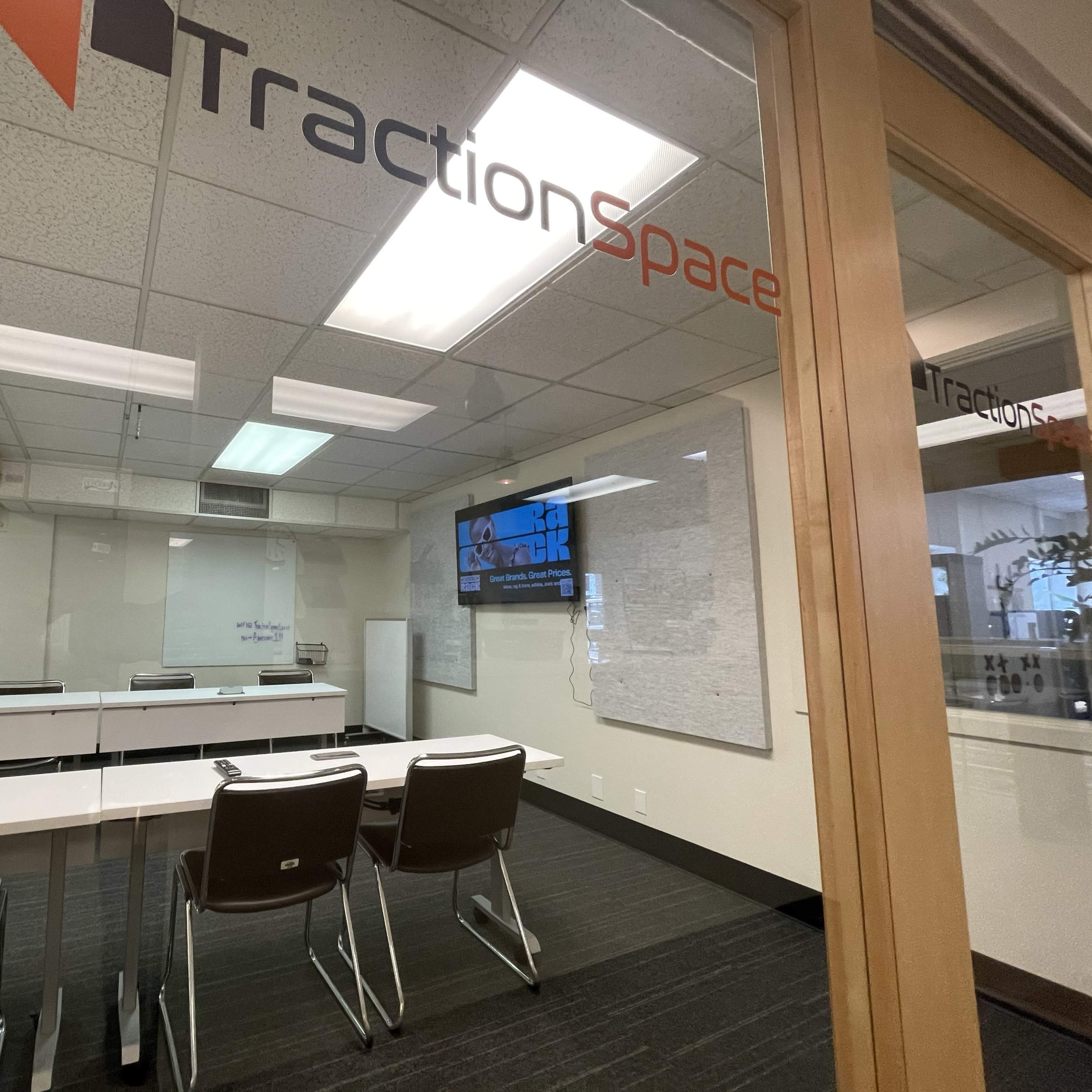 A conference room labeled "TractionSpace" with a large table and several chairs, located behind glass walls.
