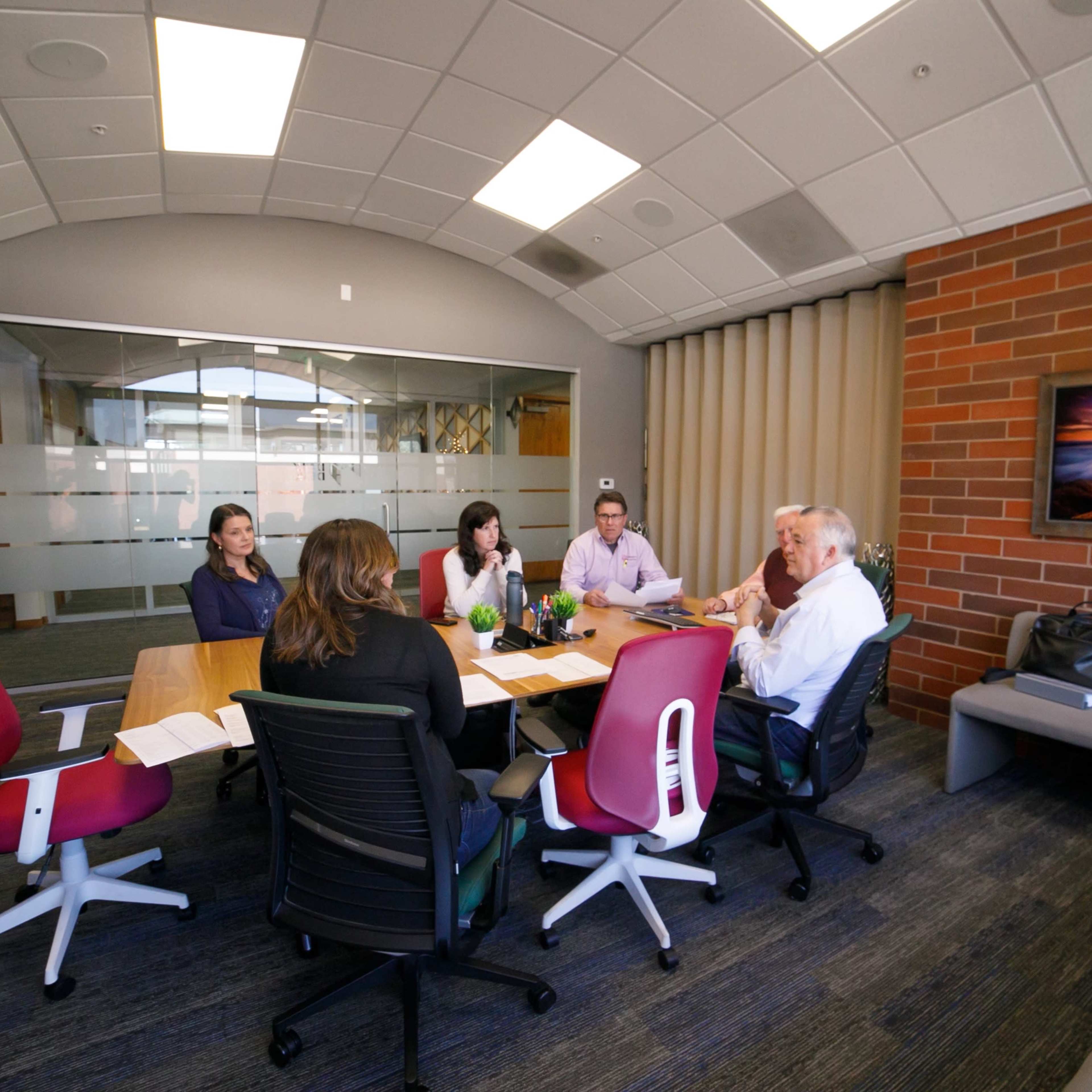 A group of five people is seated around a conference table in a modern meeting room.
