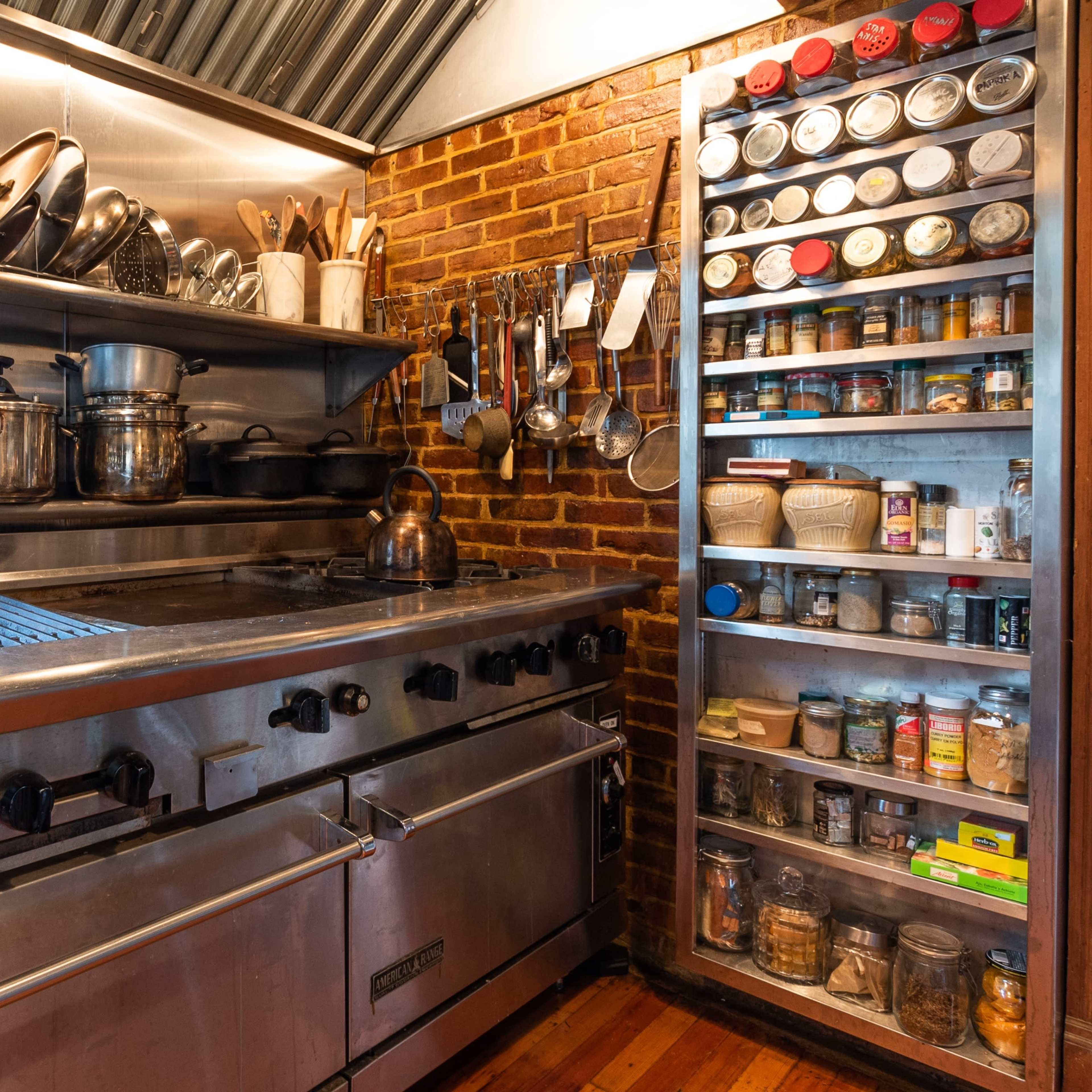 A commercial kitchen with stainless steel appliances, a grill, shelves of organized spice jars, and various cooking utensils.