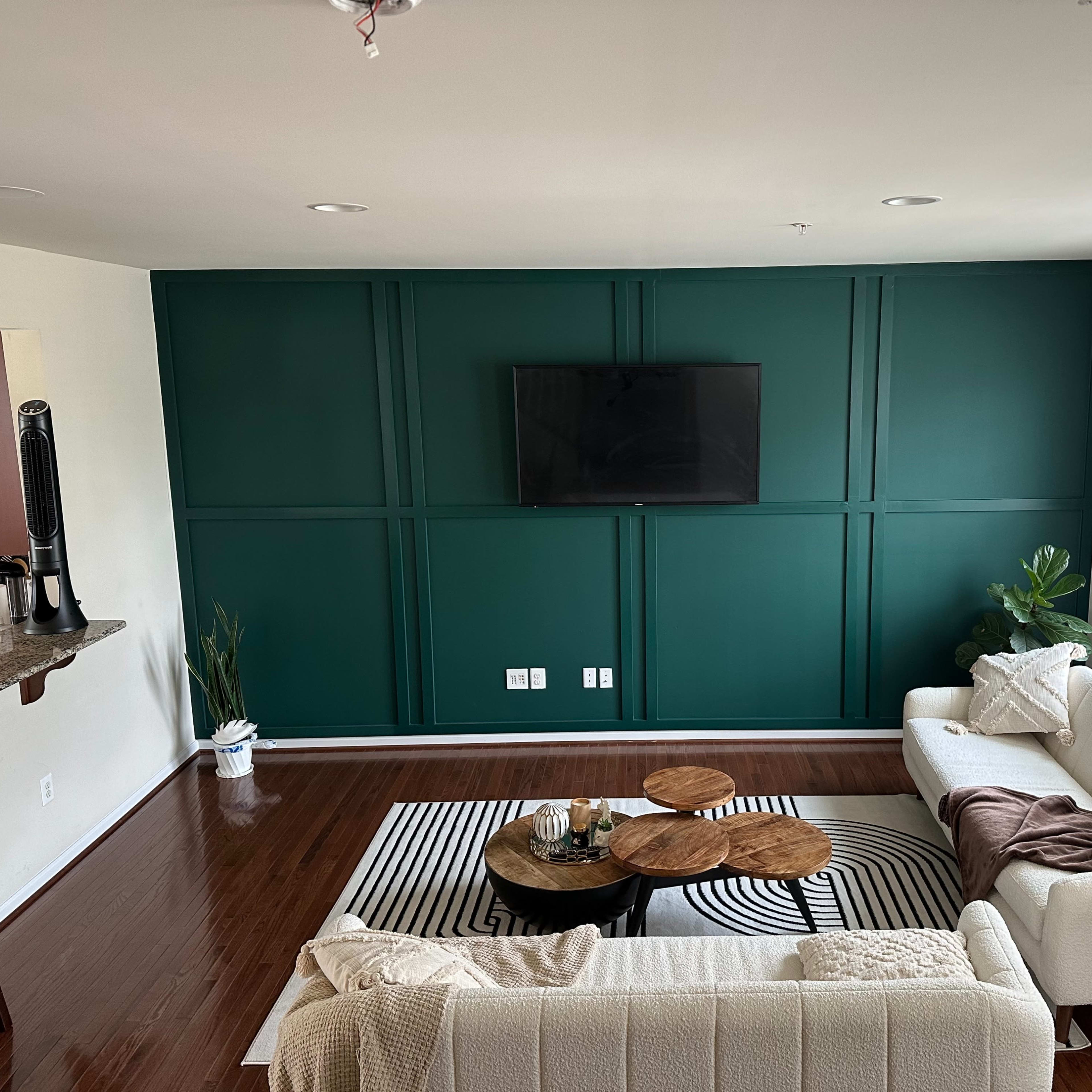 A living room with two sofas facing a dark green accent wall, a wall-mounted television, a round coffee table, and a rug with black and white stripes.