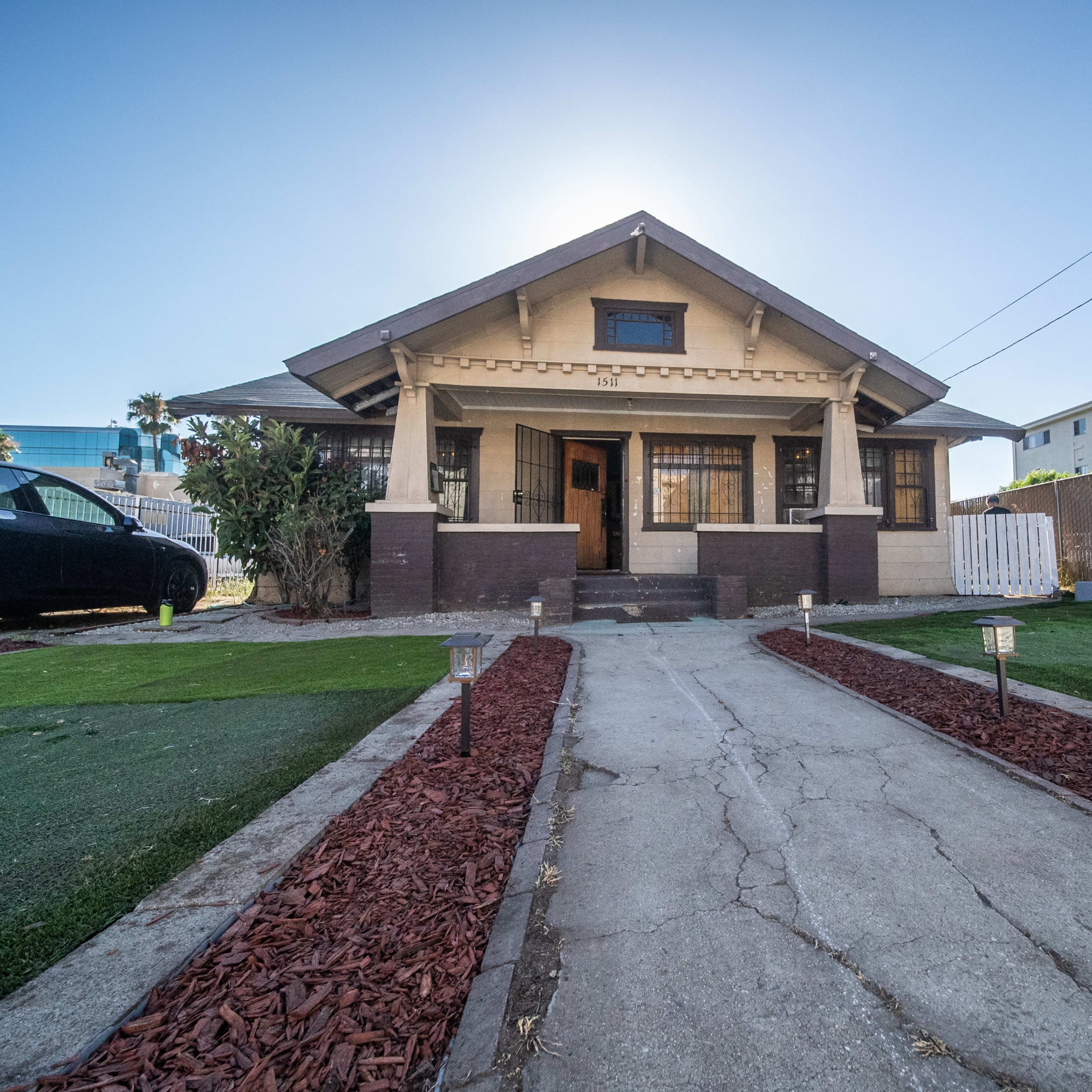 A single-story bungalow with a front walkway surrounded by landscaped grass and mulch, situated in an urban setting.
