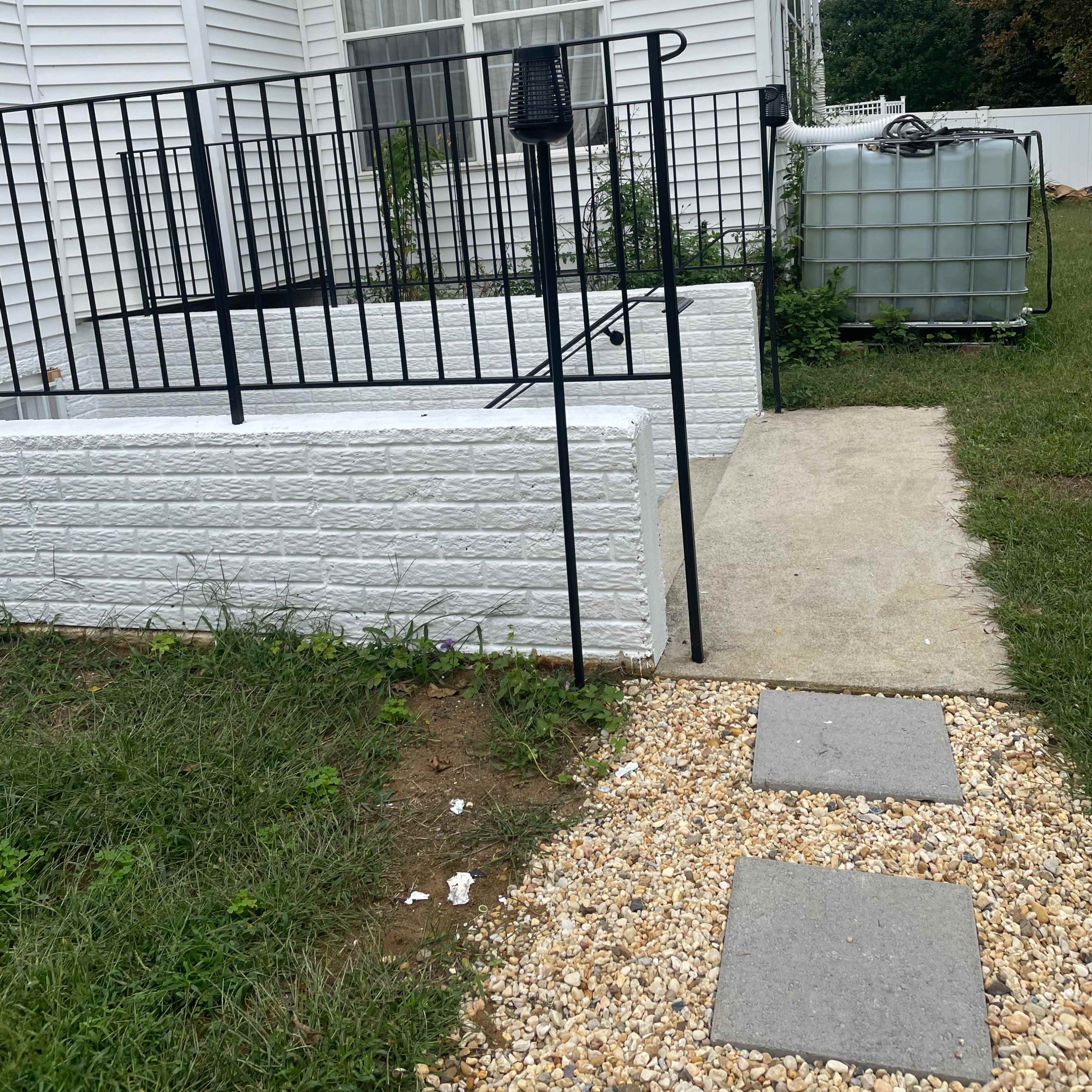 A concrete pathway leads to a white brick entryway with a black railing, beside a large water storage tank.