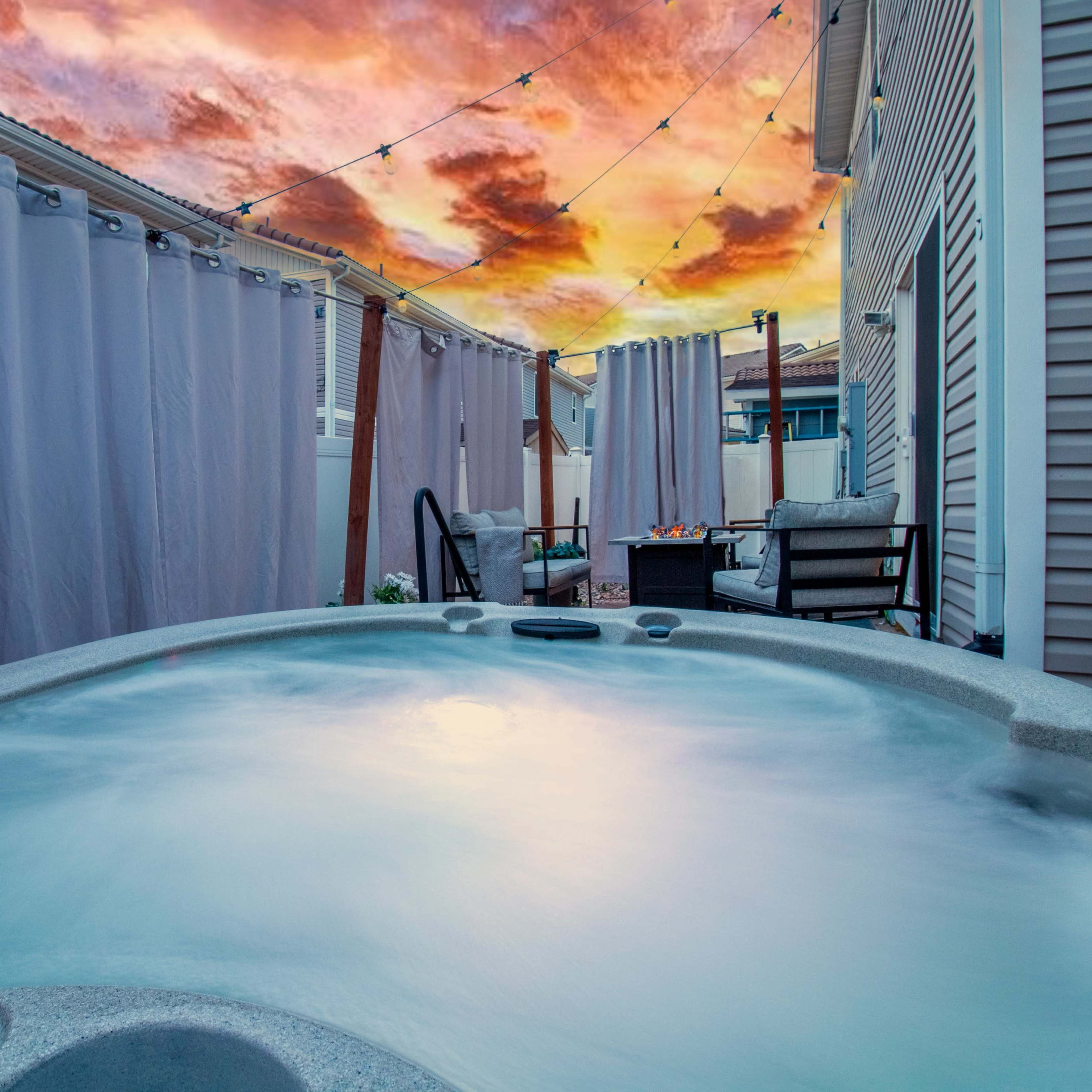 A hot tub surrounded by gray curtains and patio furniture, set against a vibrant sunset sky.