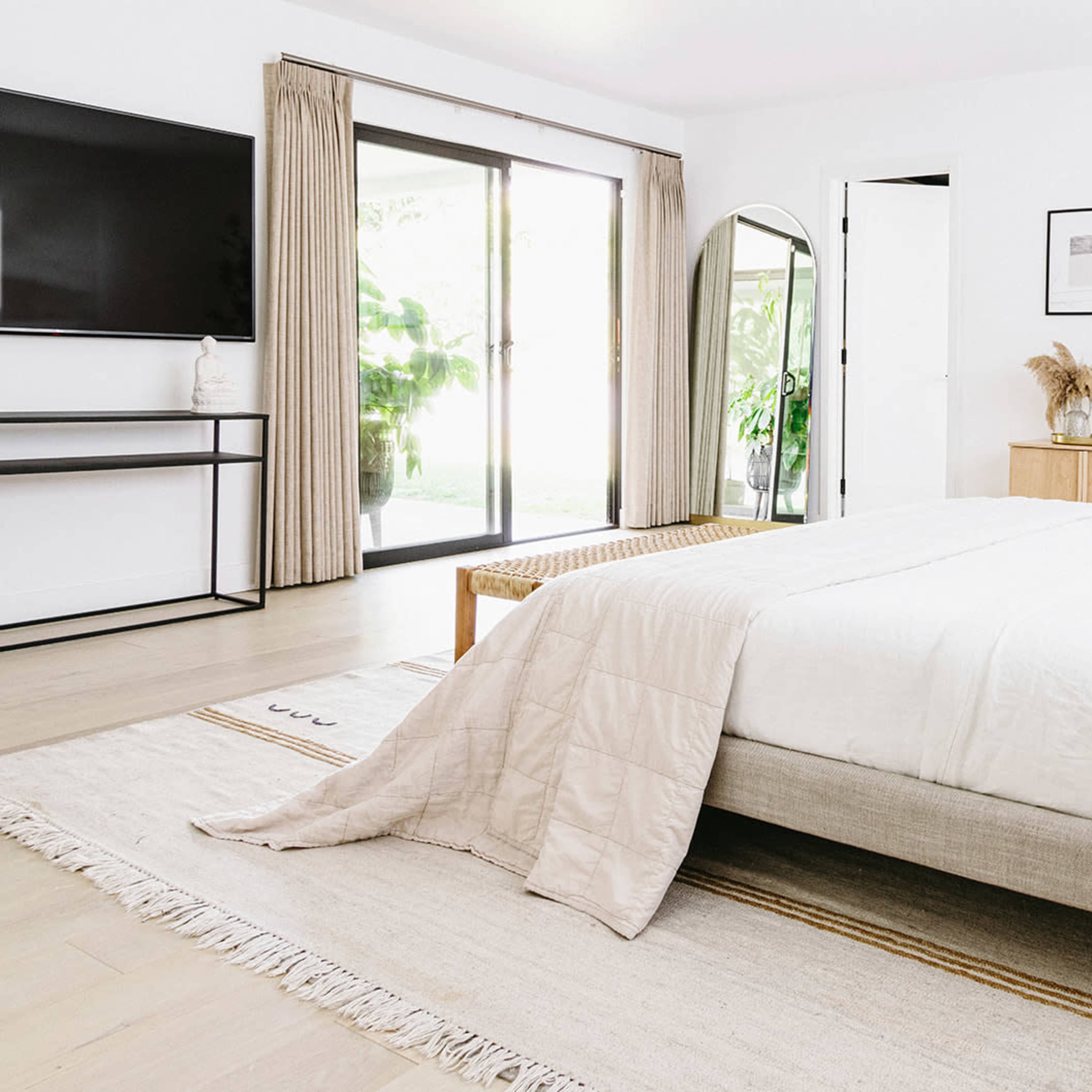 A modern bedroom featuring a large bed with white bedding, a flat-screen TV mounted on a wall, and large sliding glass doors that open to a patio.