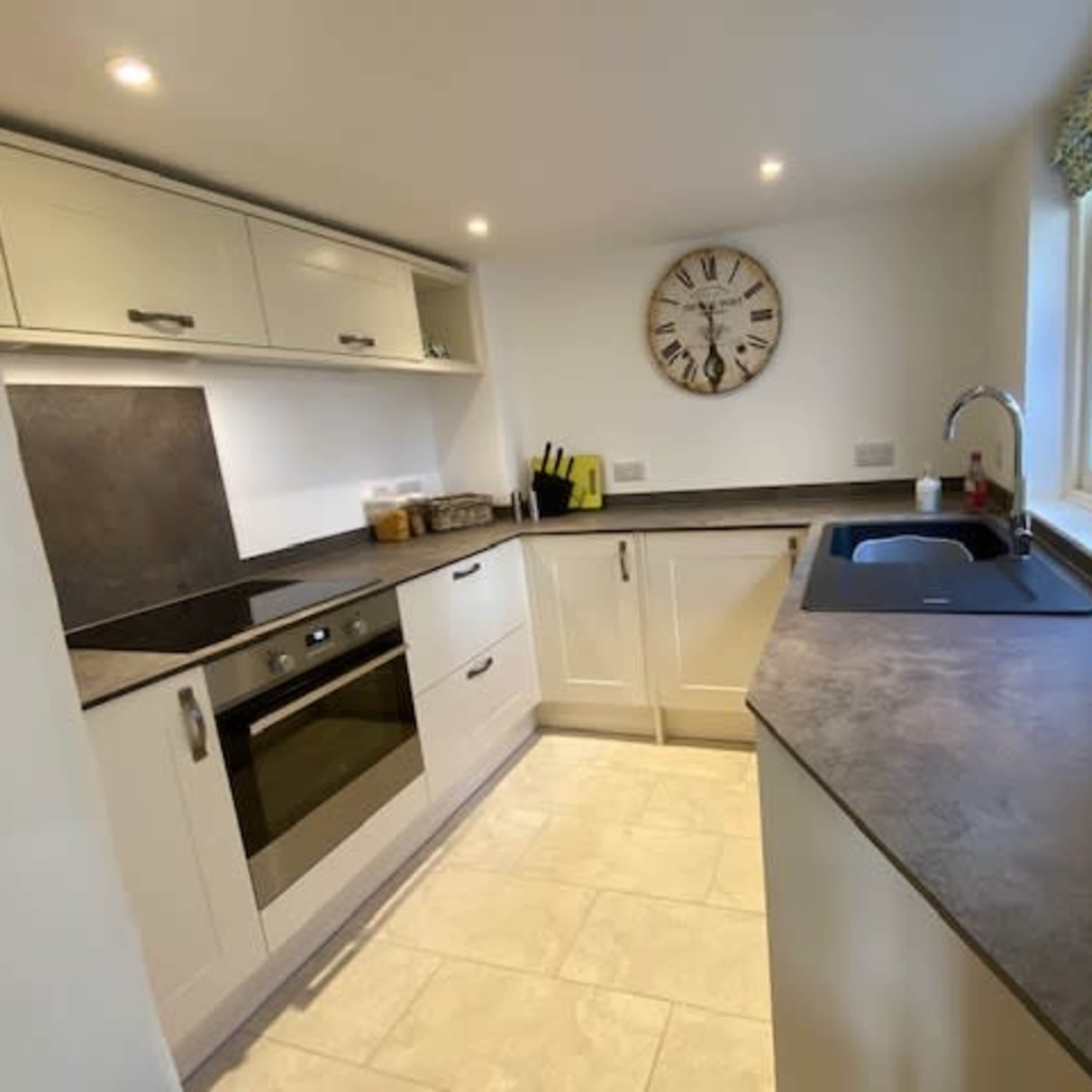 A modern kitchen with light-colored cabinets, a dark countertop, an oven, and a sink under a window.