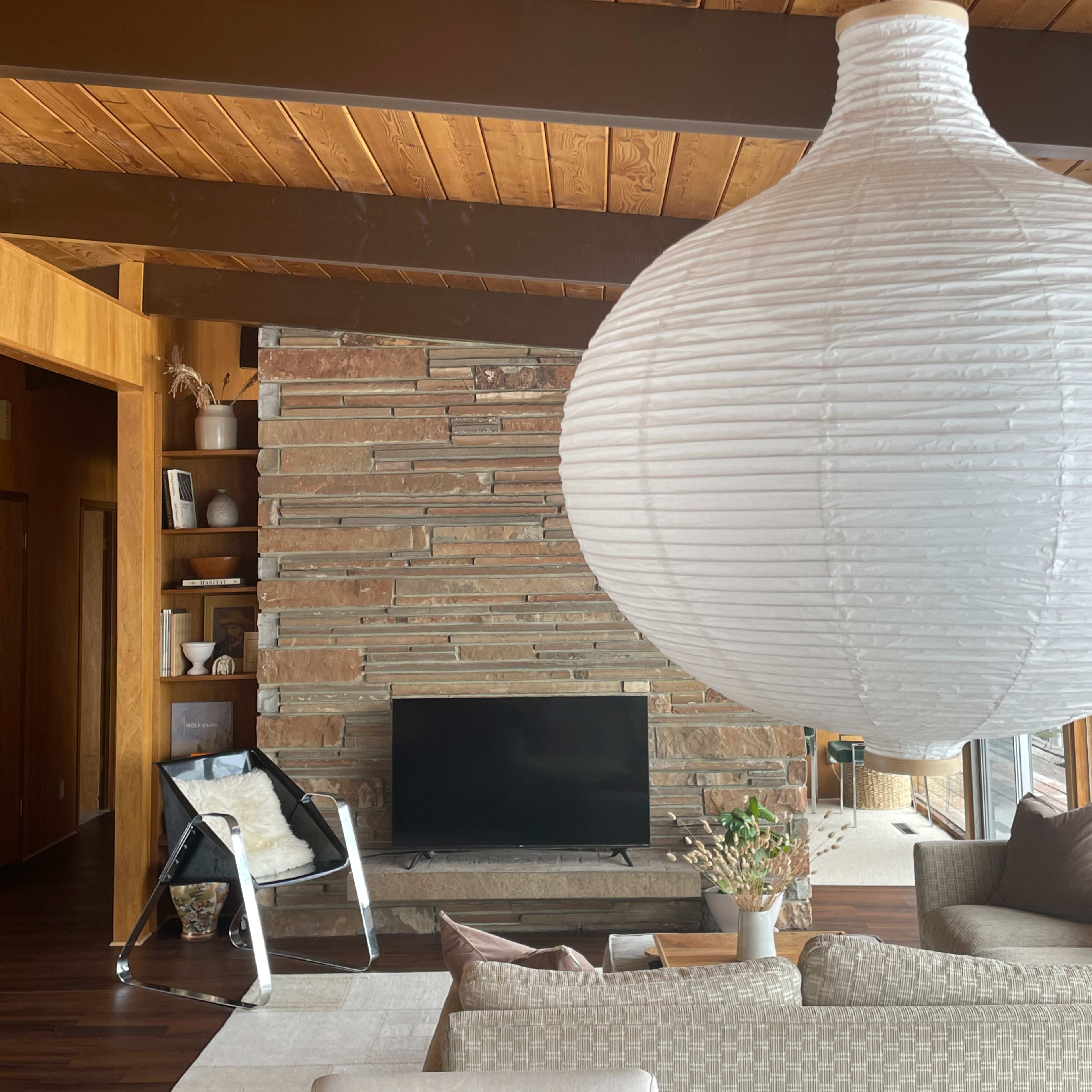 The scene features a modern living room with a stone fireplace, a television, a large hanging light fixture, and a cozy seating area.