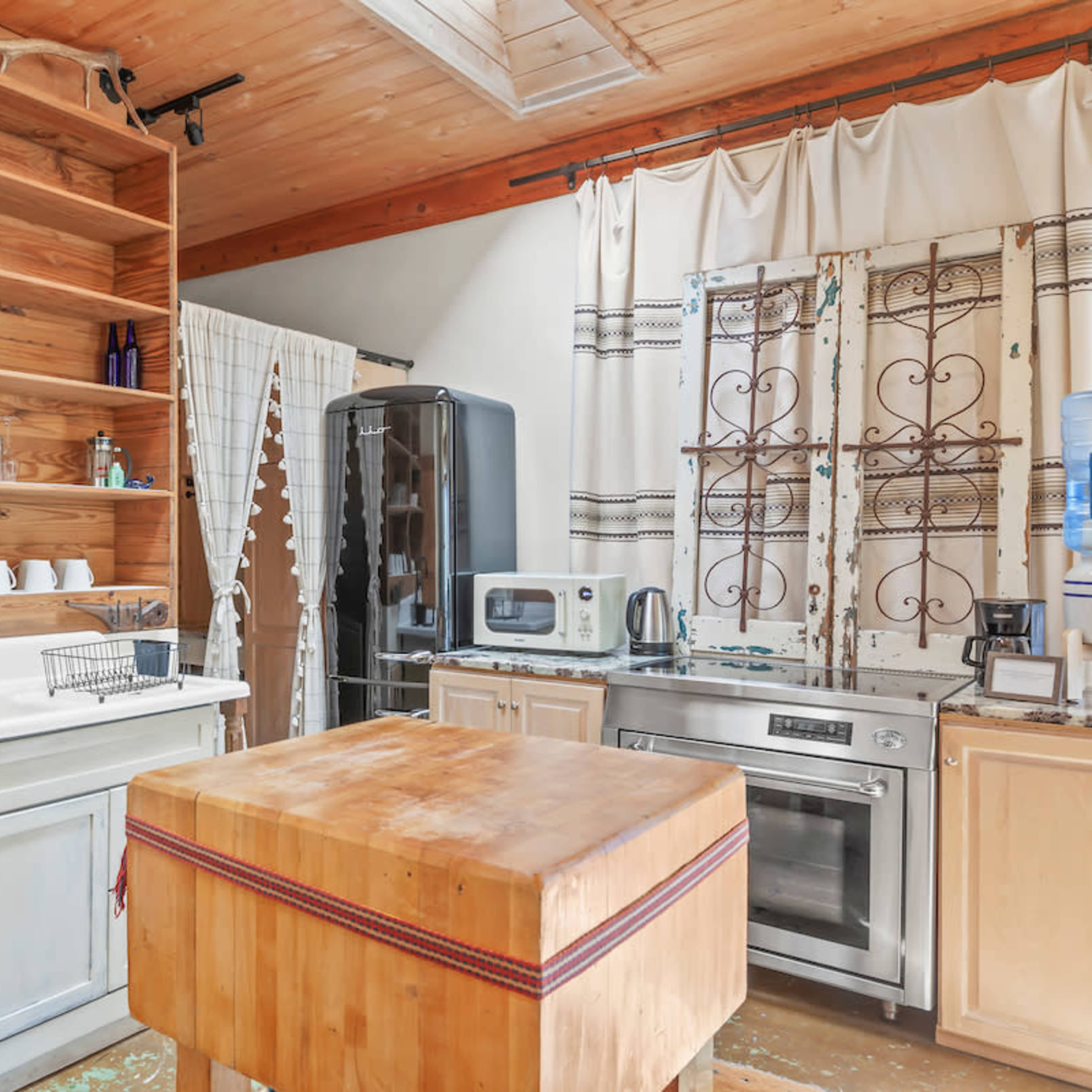 A rustic kitchen with wooden shelves, a large butcher block island, and various appliances including a refrigerator and a microwave.