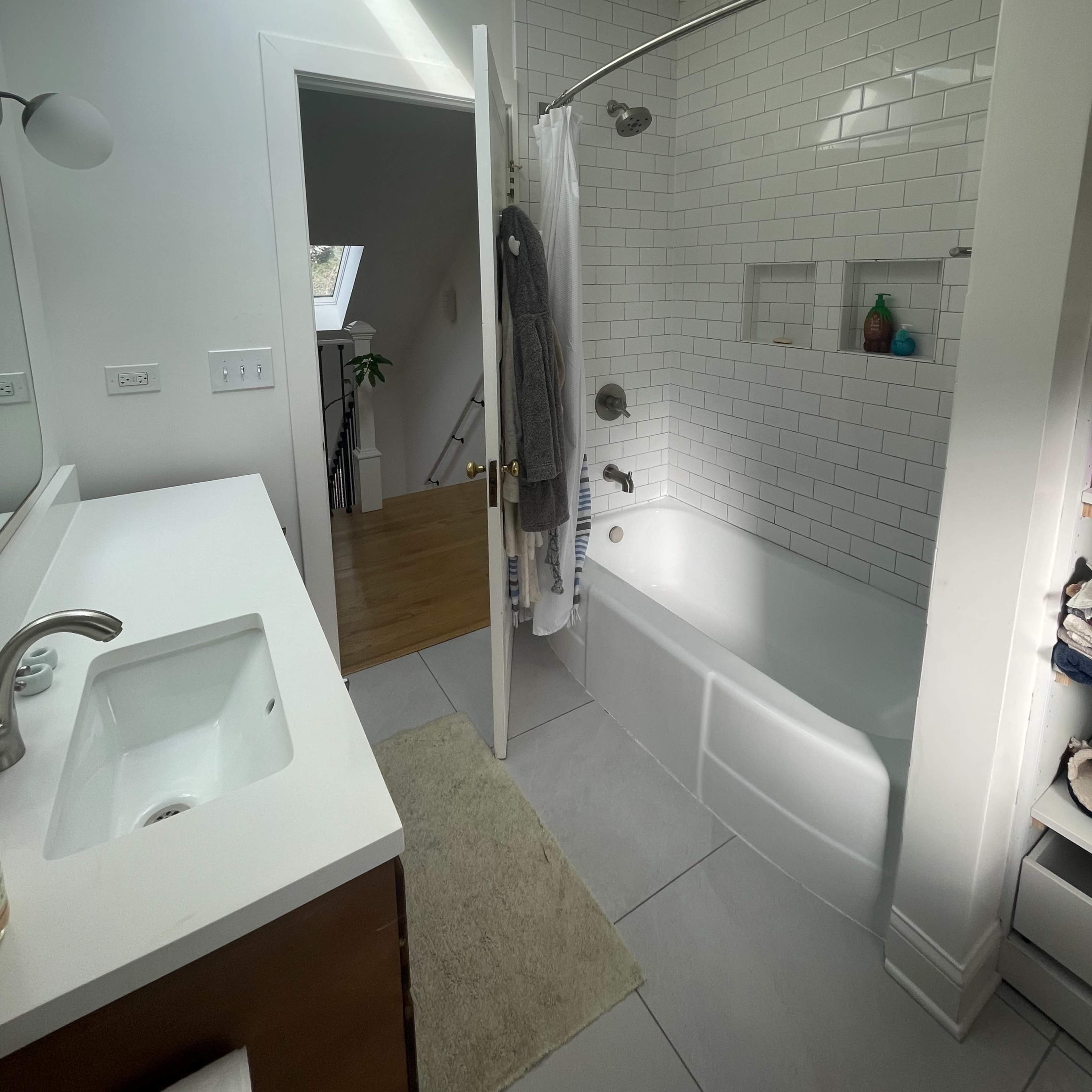 The bathroom features a bathtub with a glass shower door, a skylight, and a doorway leading to a staircase.