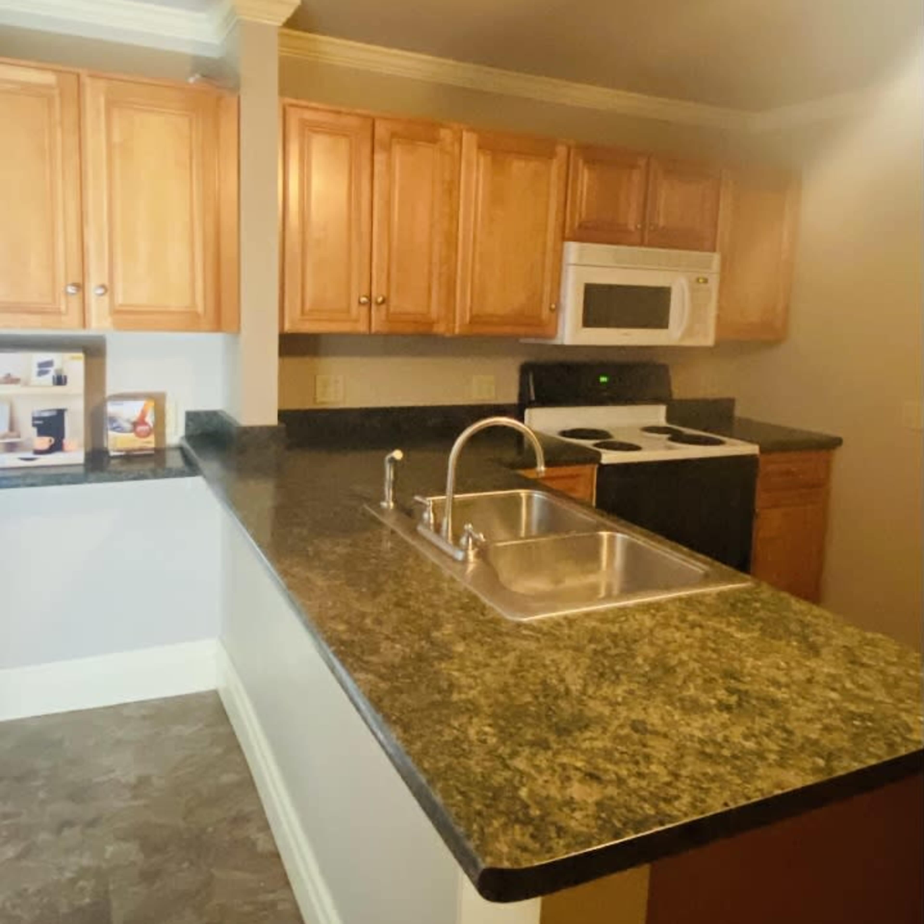 A kitchen with wooden cabinets, a black countertop, a sink, and stainless steel appliances, including a microwave and oven.