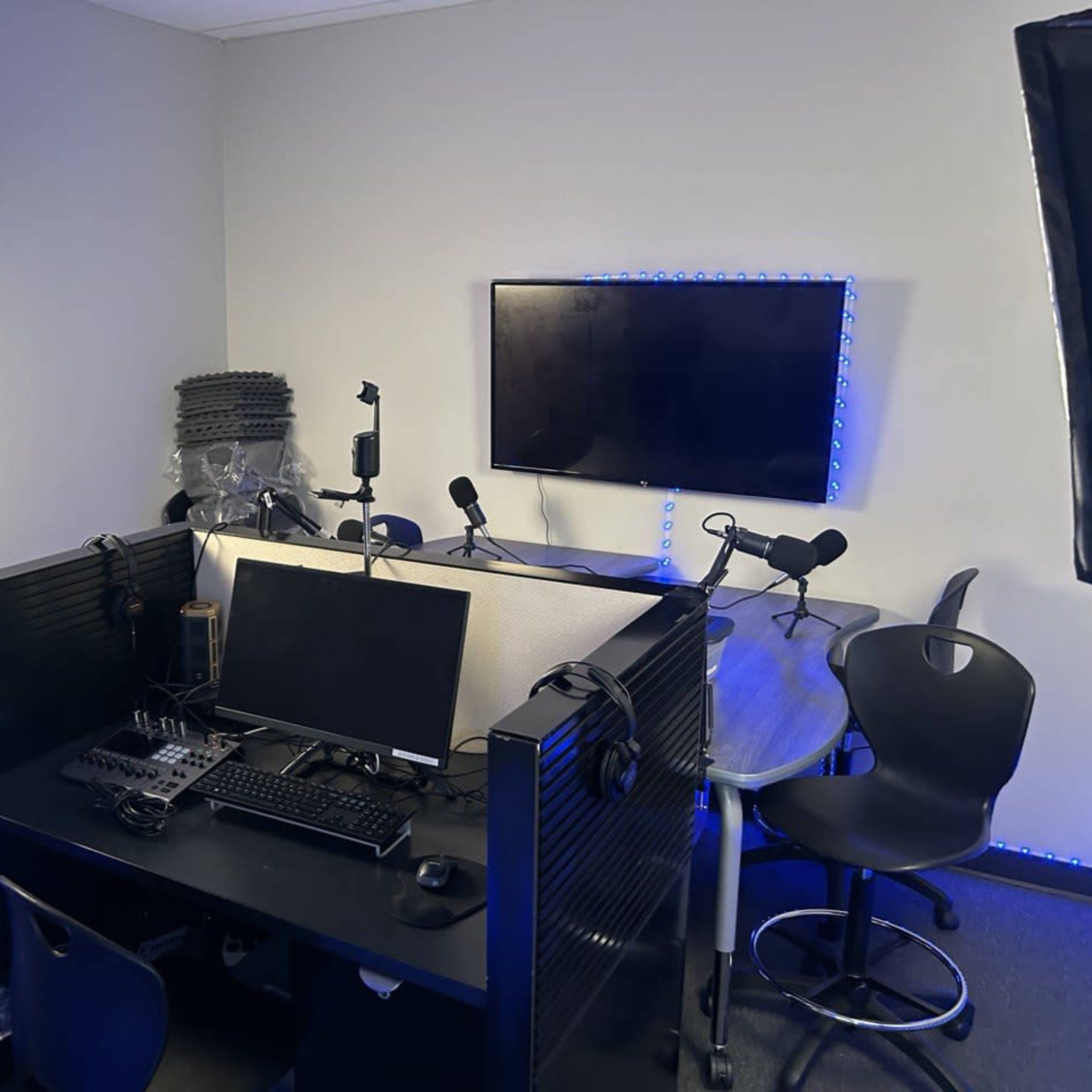 A small multimedia studio setup with a computer, microphones, and lighting equipment, arranged for recording or broadcasting.