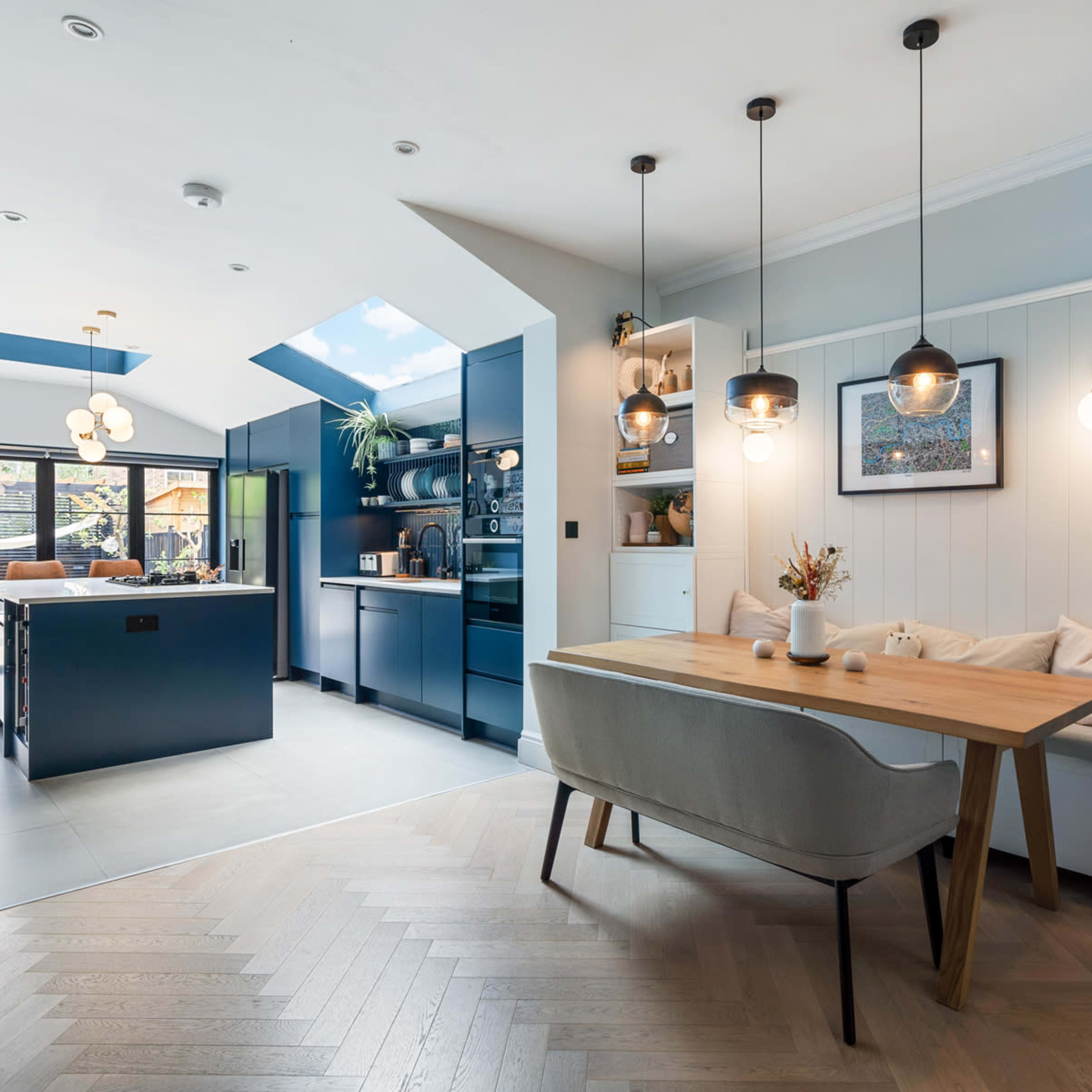A modern kitchen and dining area features an island with bar seating, suspended light fixtures, and a large window that provides natural light.