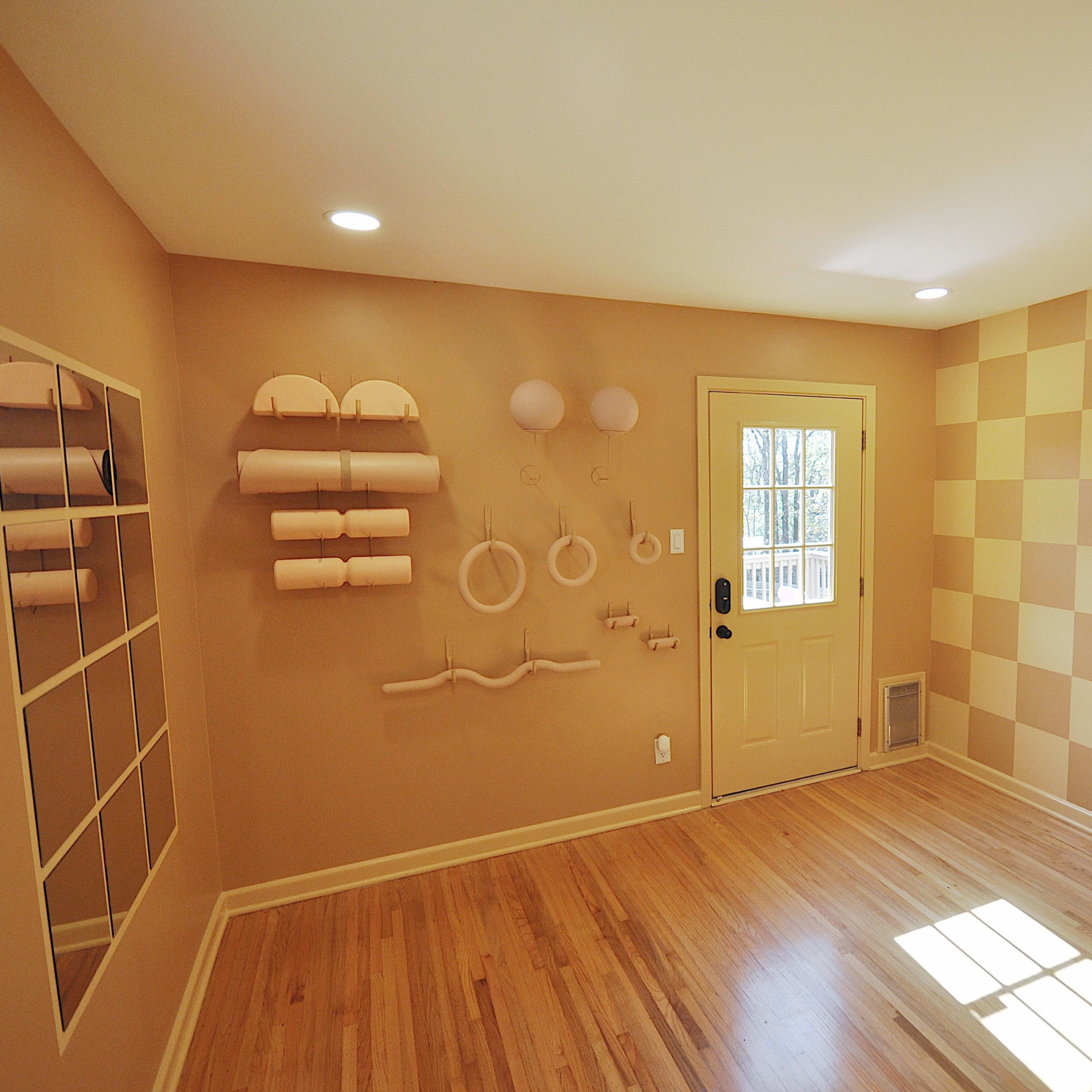 The room features a beige and yellow checkered wall, a door leading outside, and several decorative wall-mounted items alongside a large mirror.