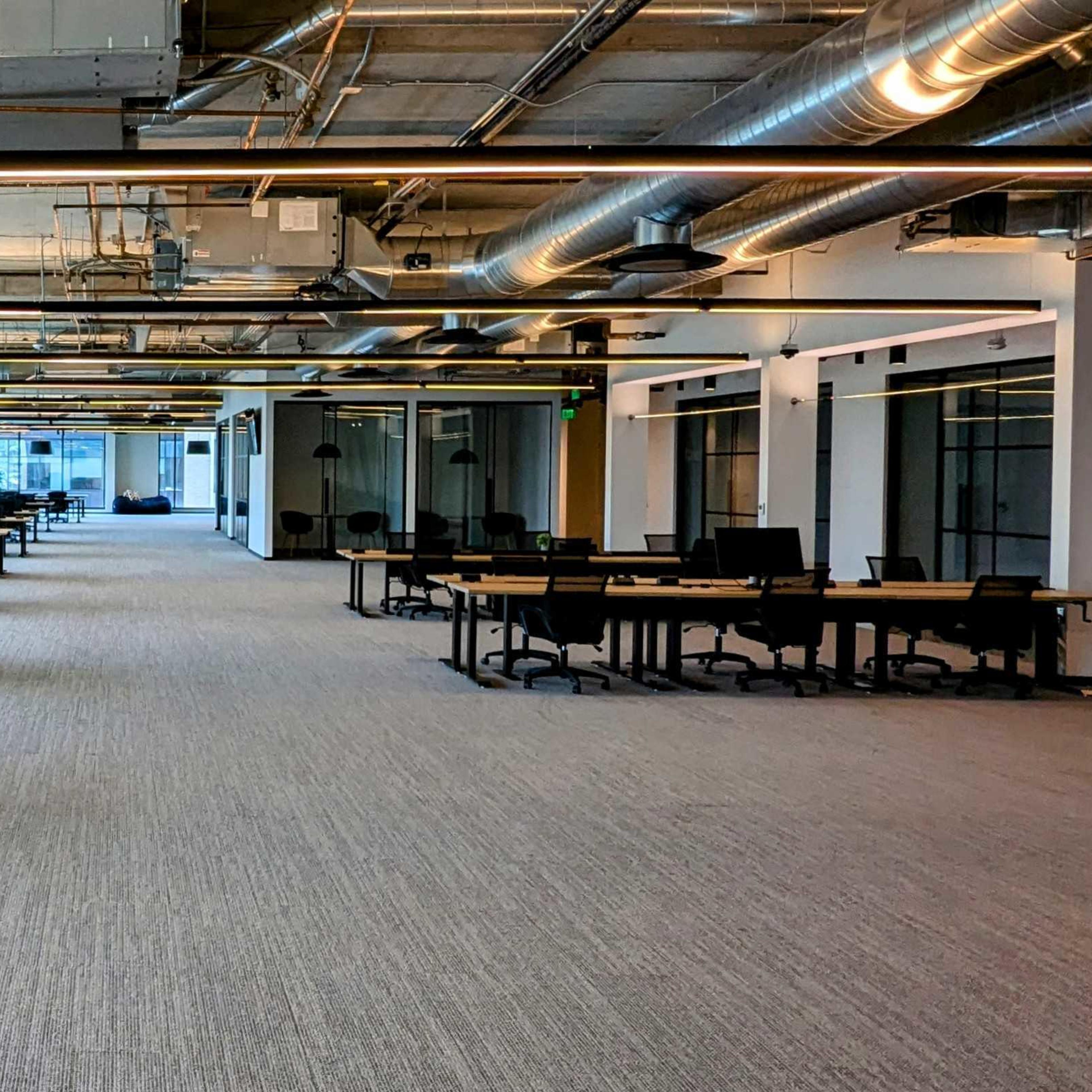 A spacious, modern office environment with rows of empty desks and large windows allowing natural light to enter.