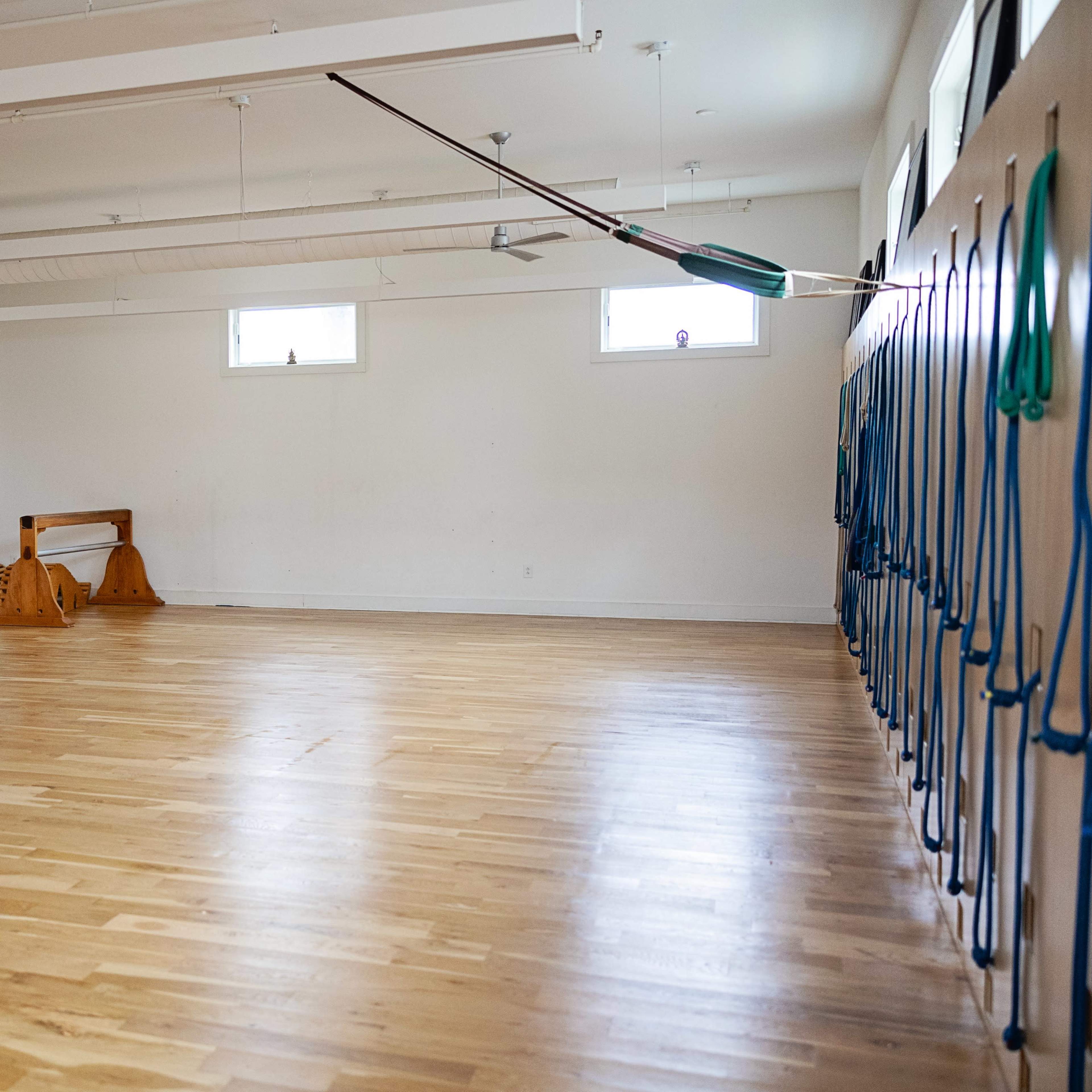 A spacious, empty room with wooden flooring and exercise equipment along the walls.
