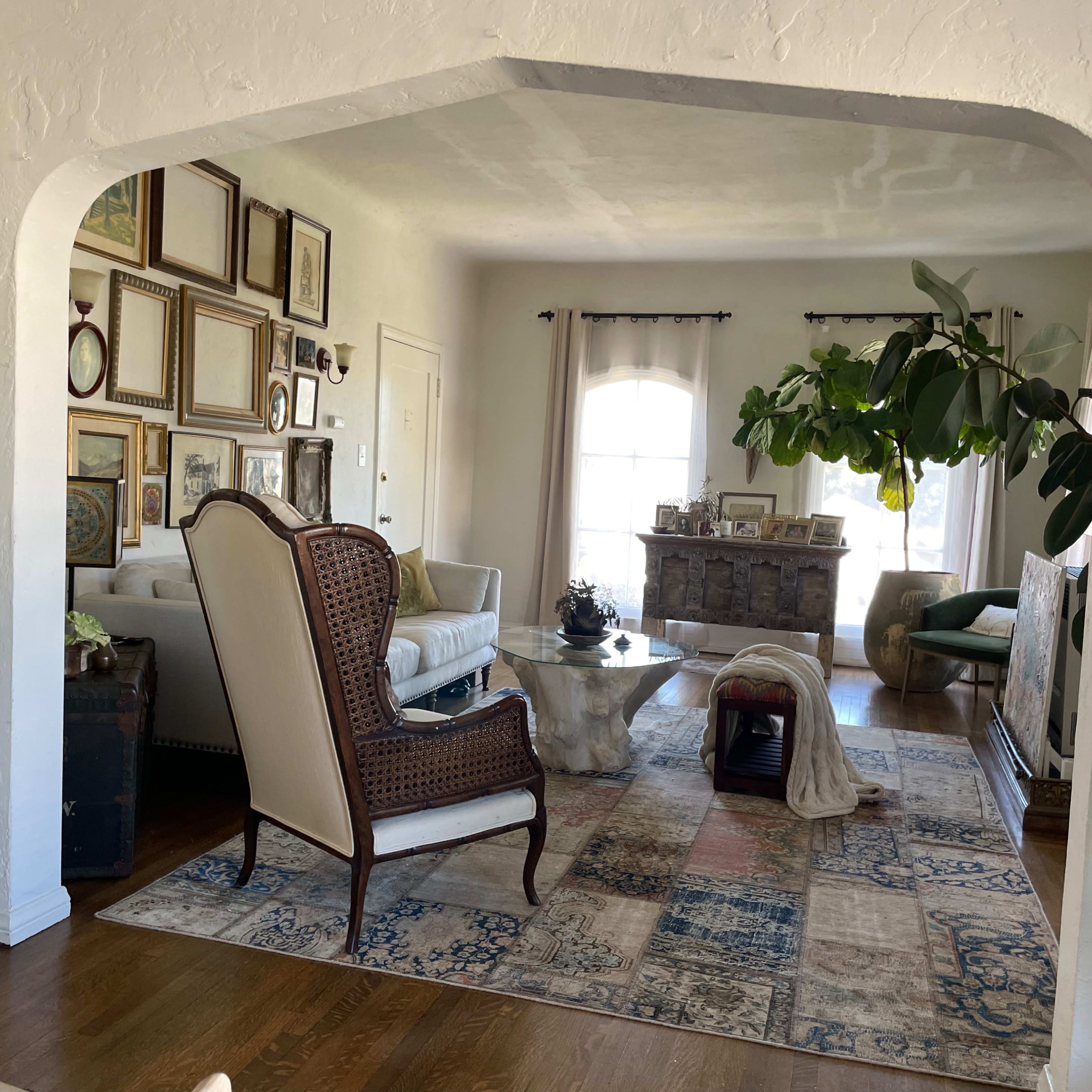A cozy living room with a framed gallery wall, a patterned rug, and a large window allowing natural light to enter.