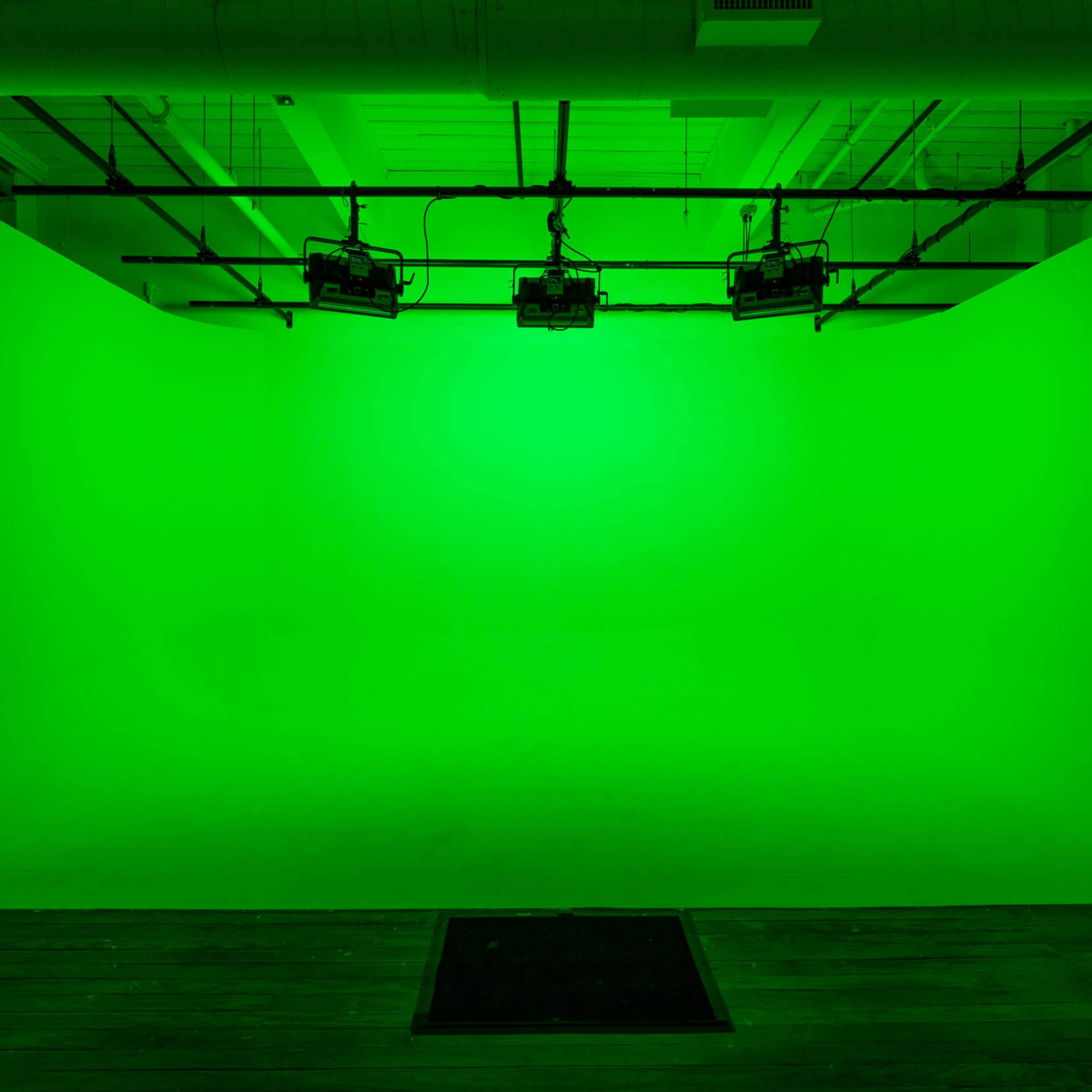 A green screen backdrop illuminated by overhead lights in a studio setting.