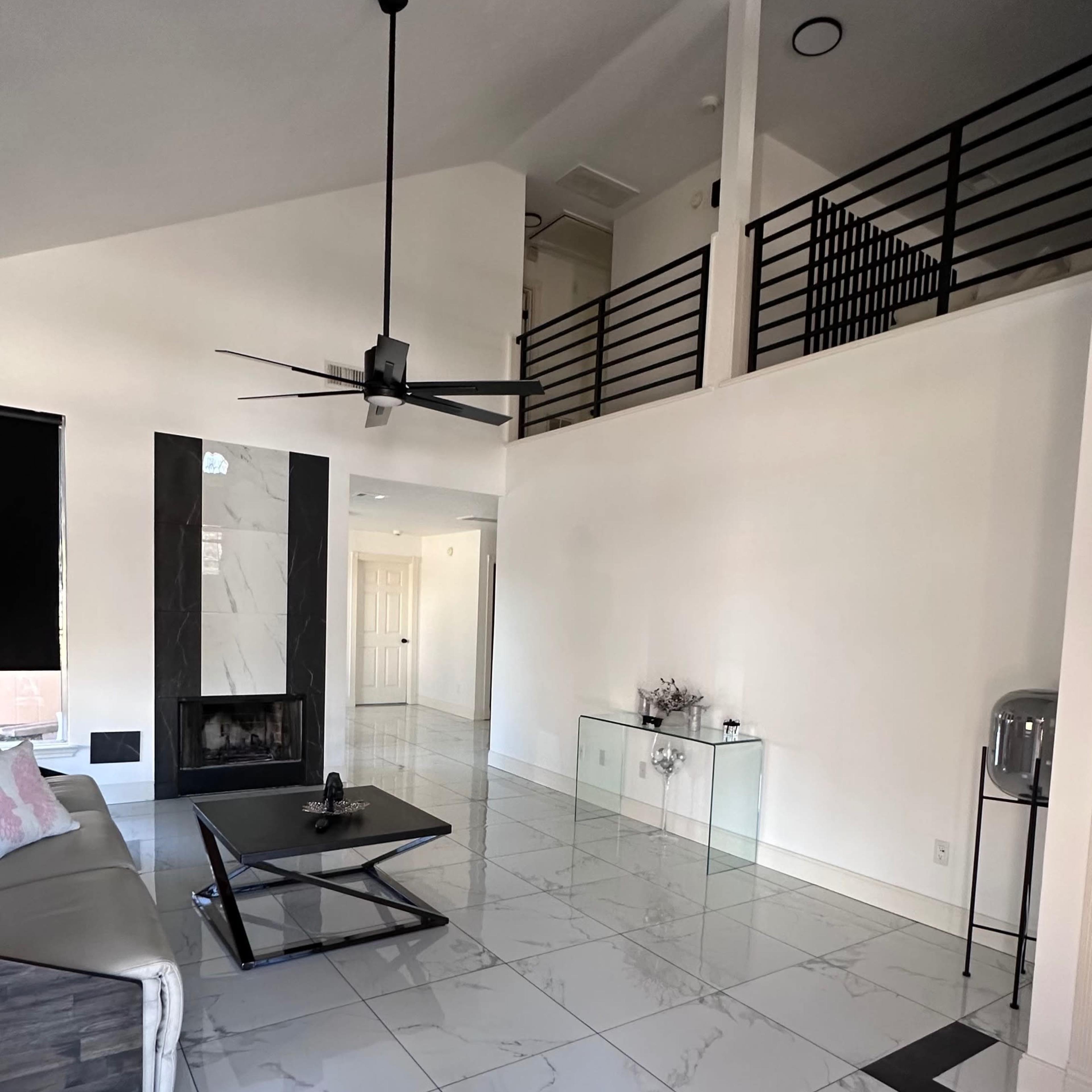A modern living room featuring a large marble-tiled floor, a fireplace, a ceiling fan, and a staircase leading to a second level.