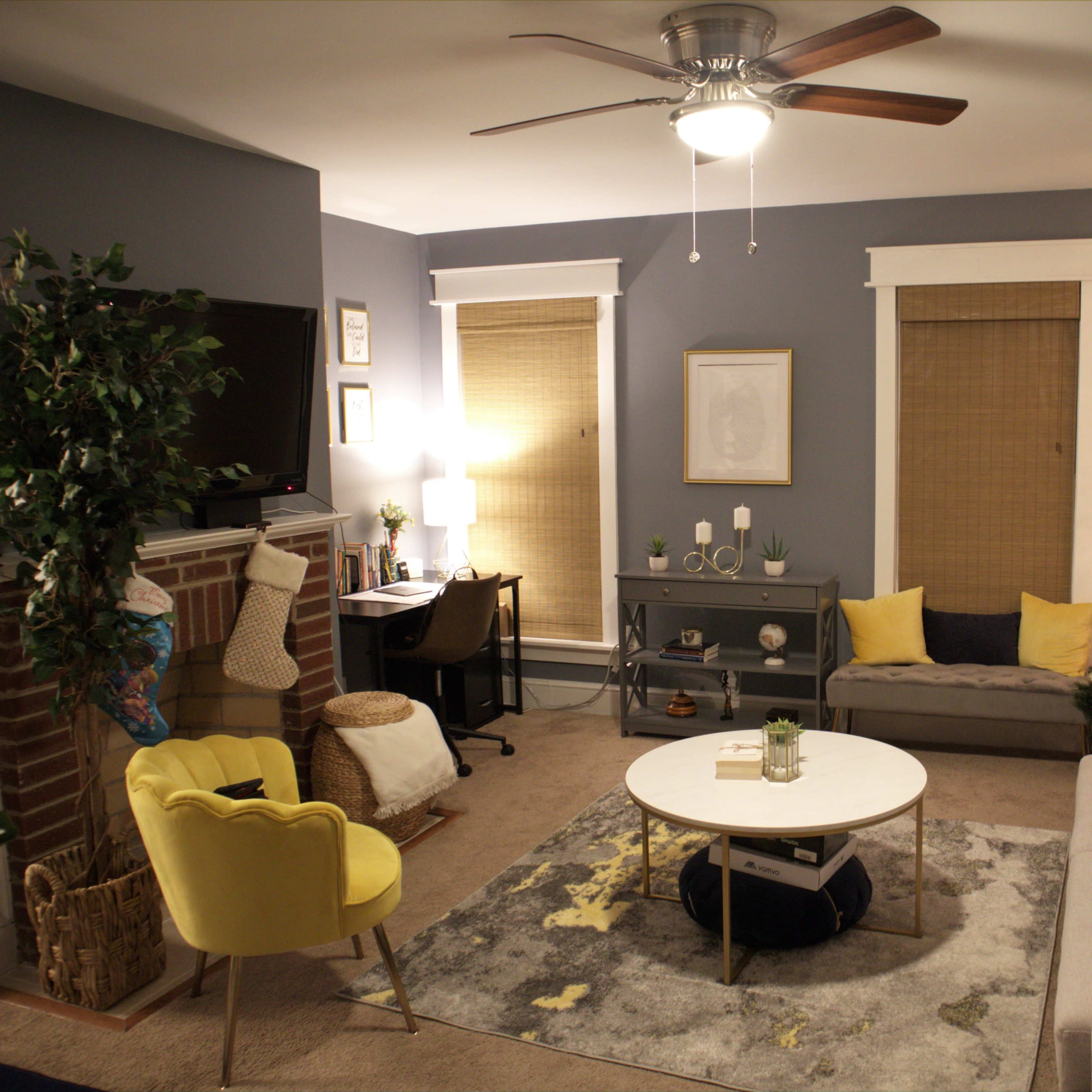 A cozy living room features a Christmas tree, a sofa, a coffee table, and a workspace beside a fireplace.
