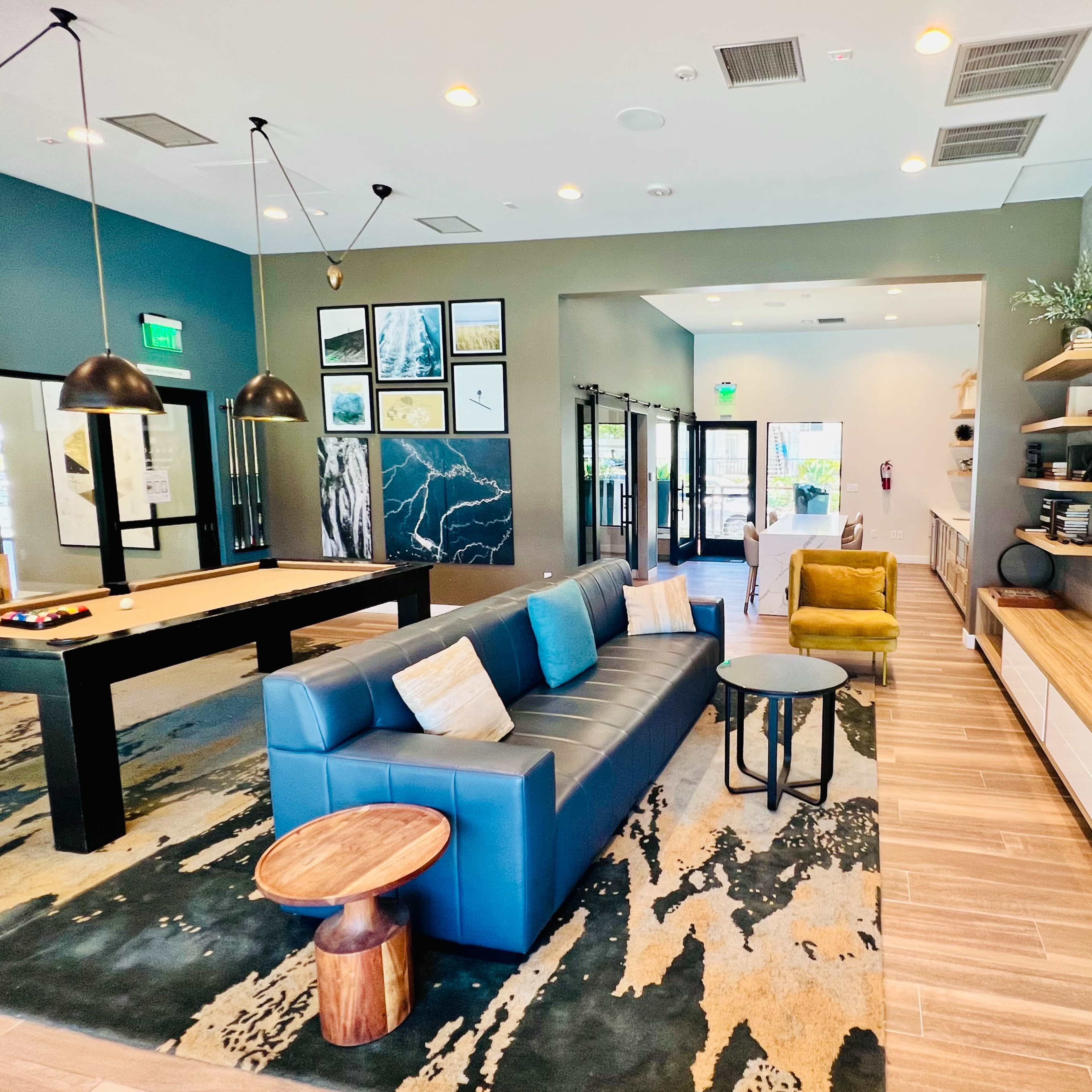 A modern lobby with a blue sofa, yellow chair, pool table, and a wall-mounted television surrounded by bookshelves.