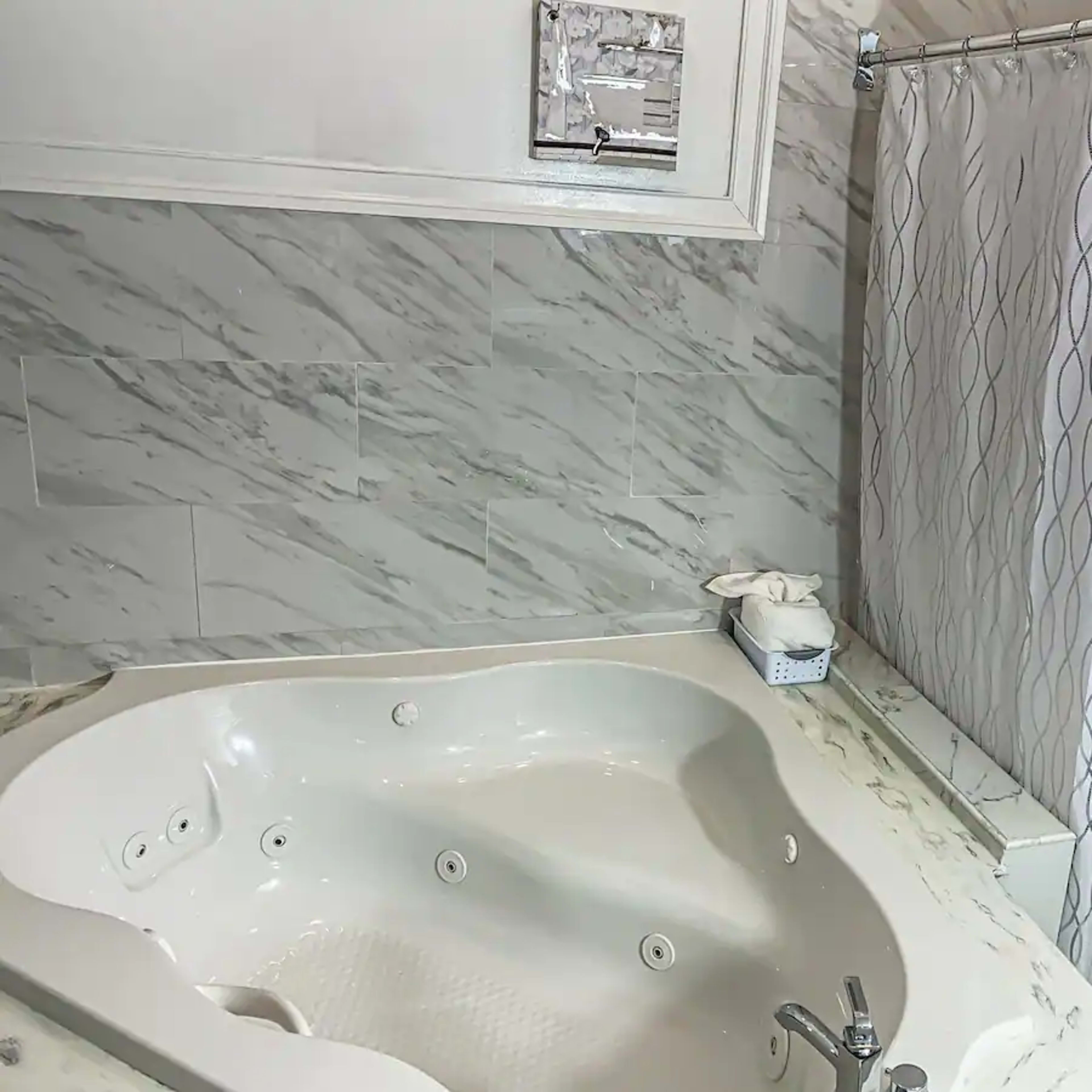 A corner of a bathroom featuring a large, white jacuzzi tub next to a shower with a patterned curtain.