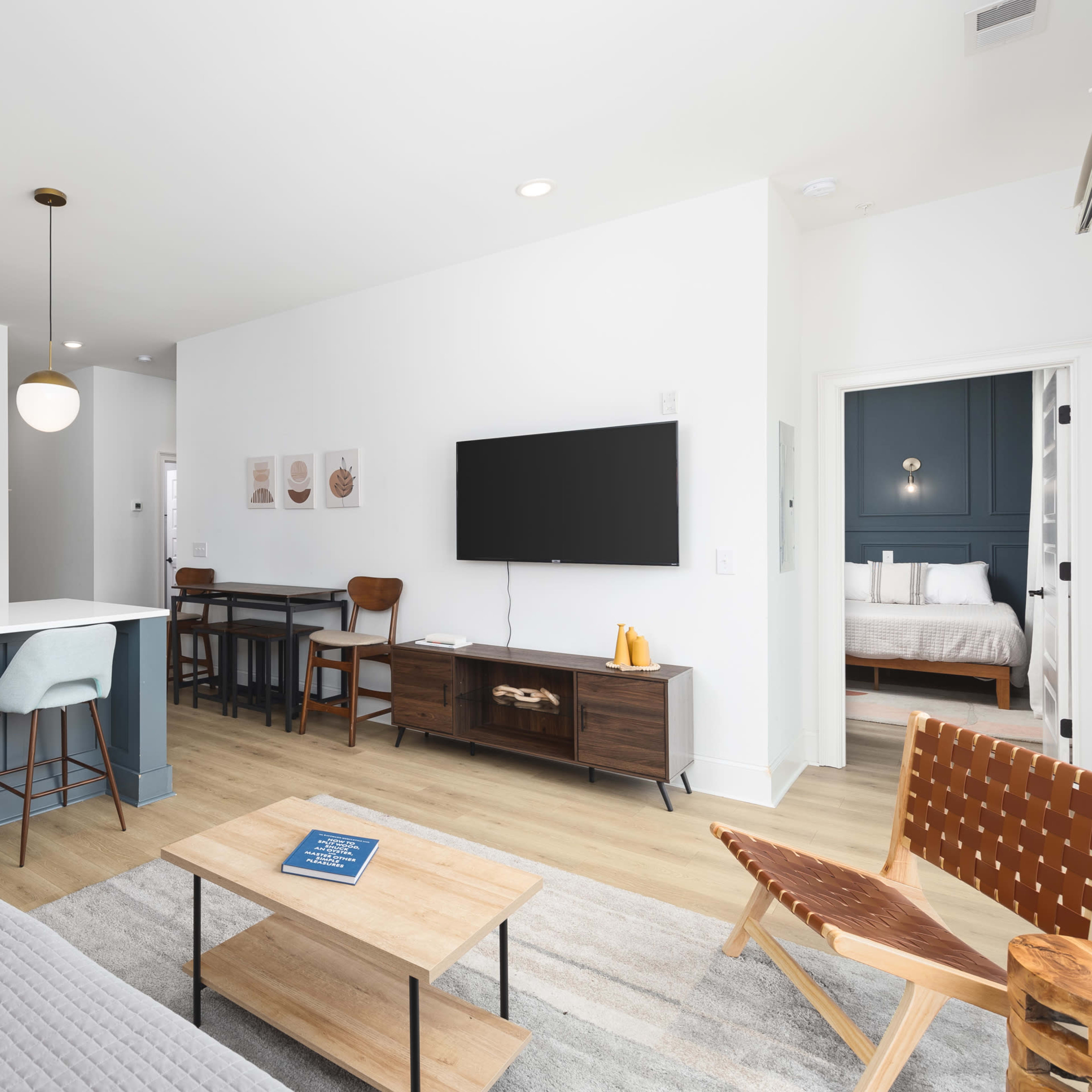 A modern living space features a kitchen with a blue island, a dining area, and a lounge area with a television and a coffee table.