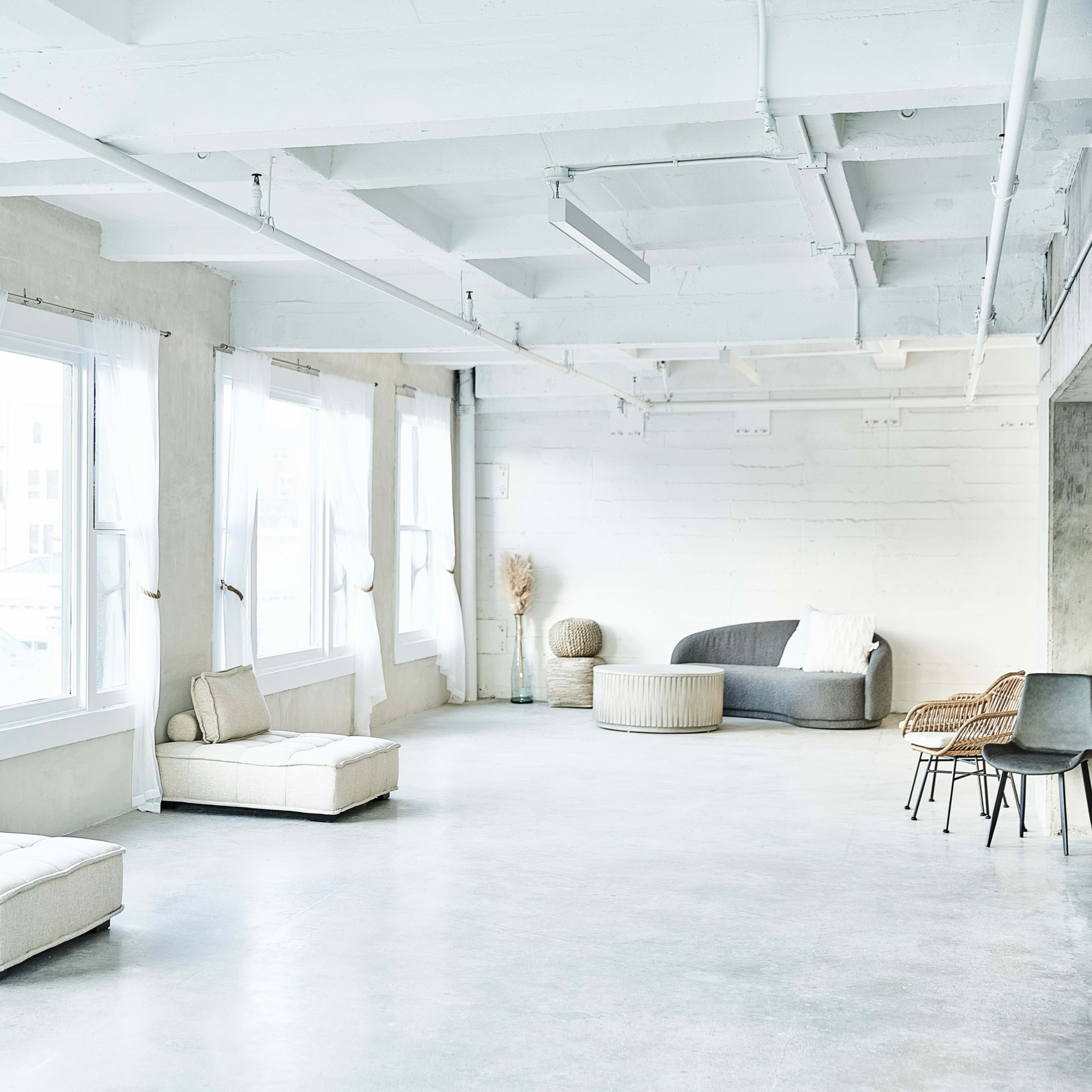 A spacious, well-lit room with large windows, minimalist furniture, and a neutral color palette.