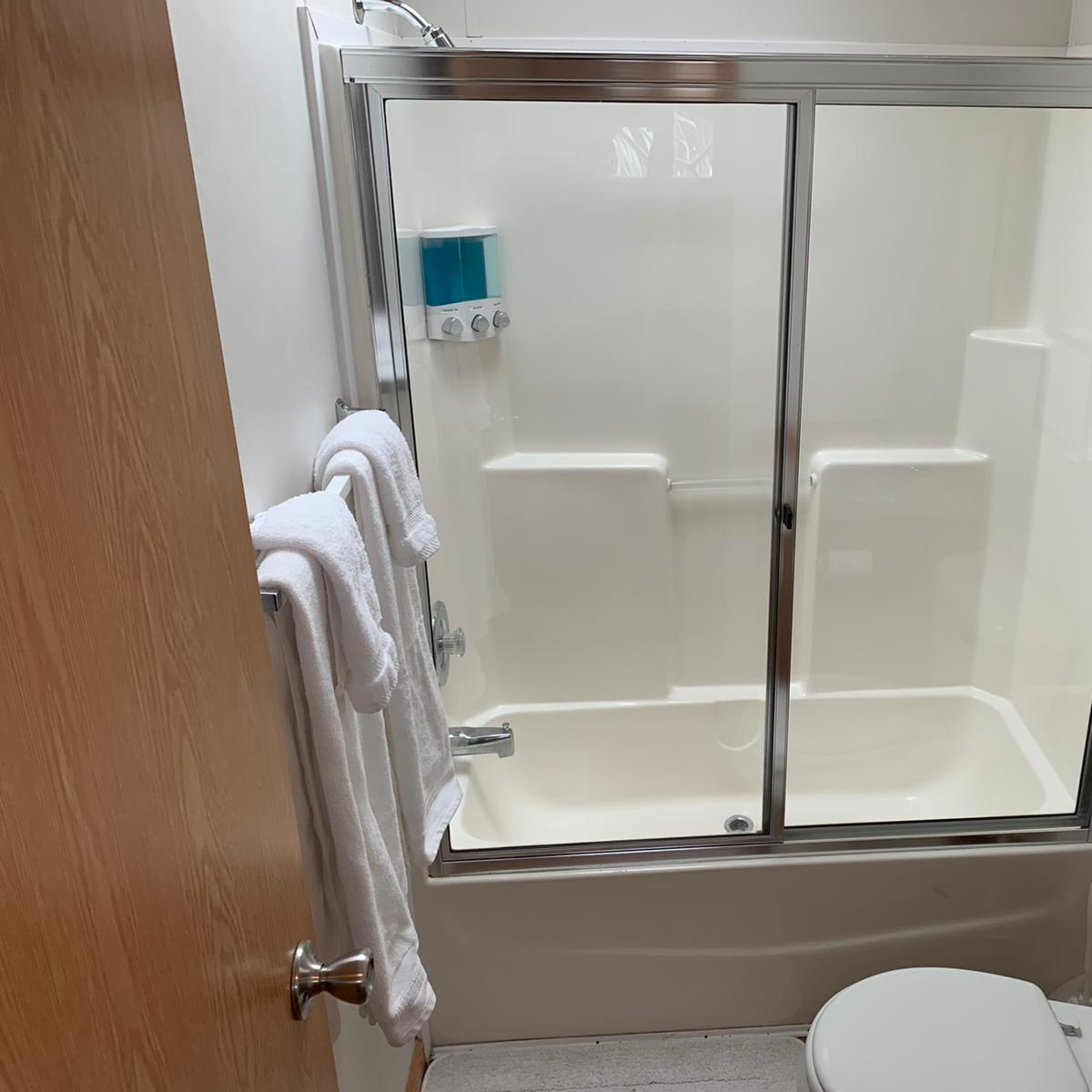 A clean bathroom with a shower enclosed by glass doors, a toilet, and neatly hung towels.