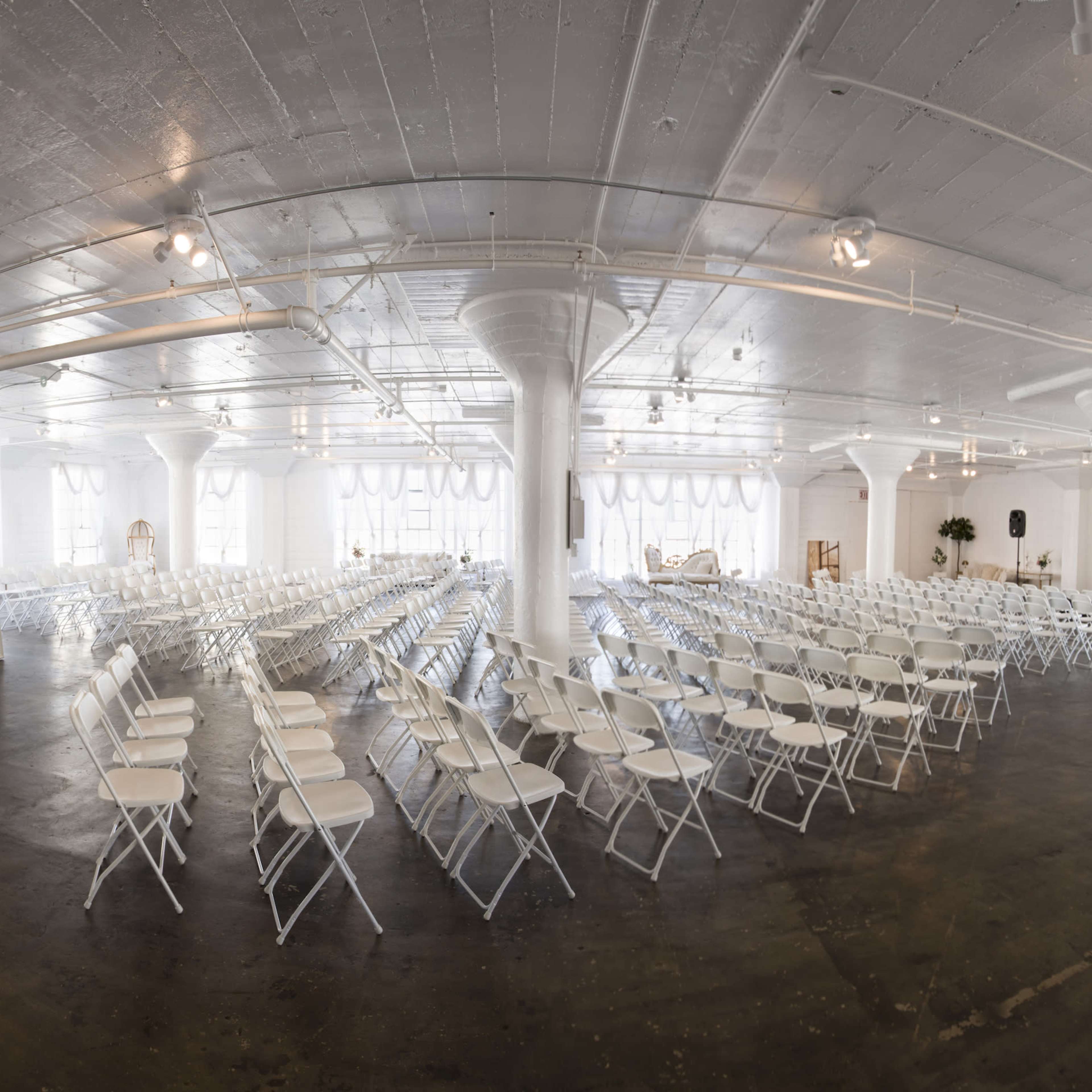 A large, empty event space set up with rows of white folding chairs arranged for an event.