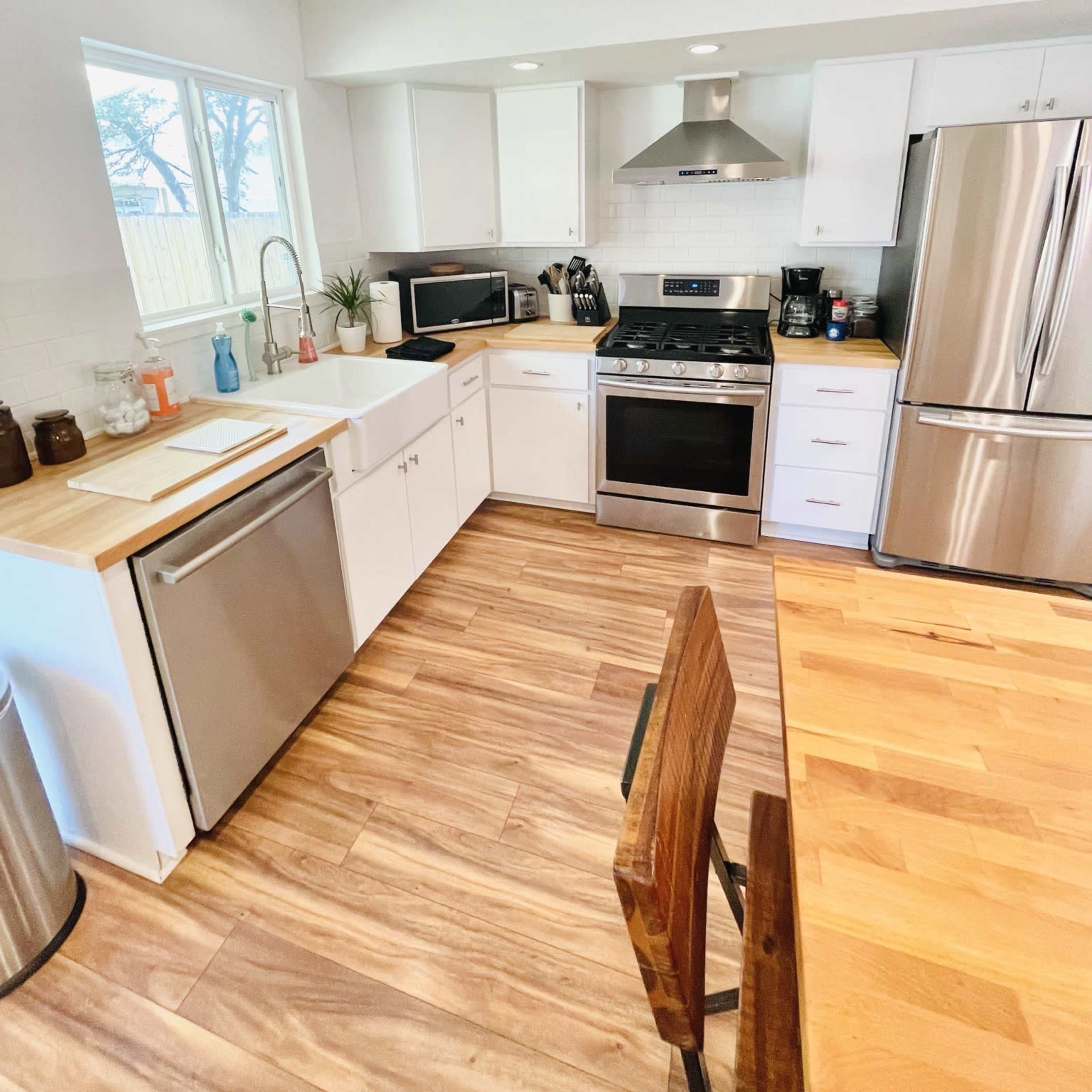 A modern kitchen with white cabinets, stainless steel appliances, and wooden flooring.