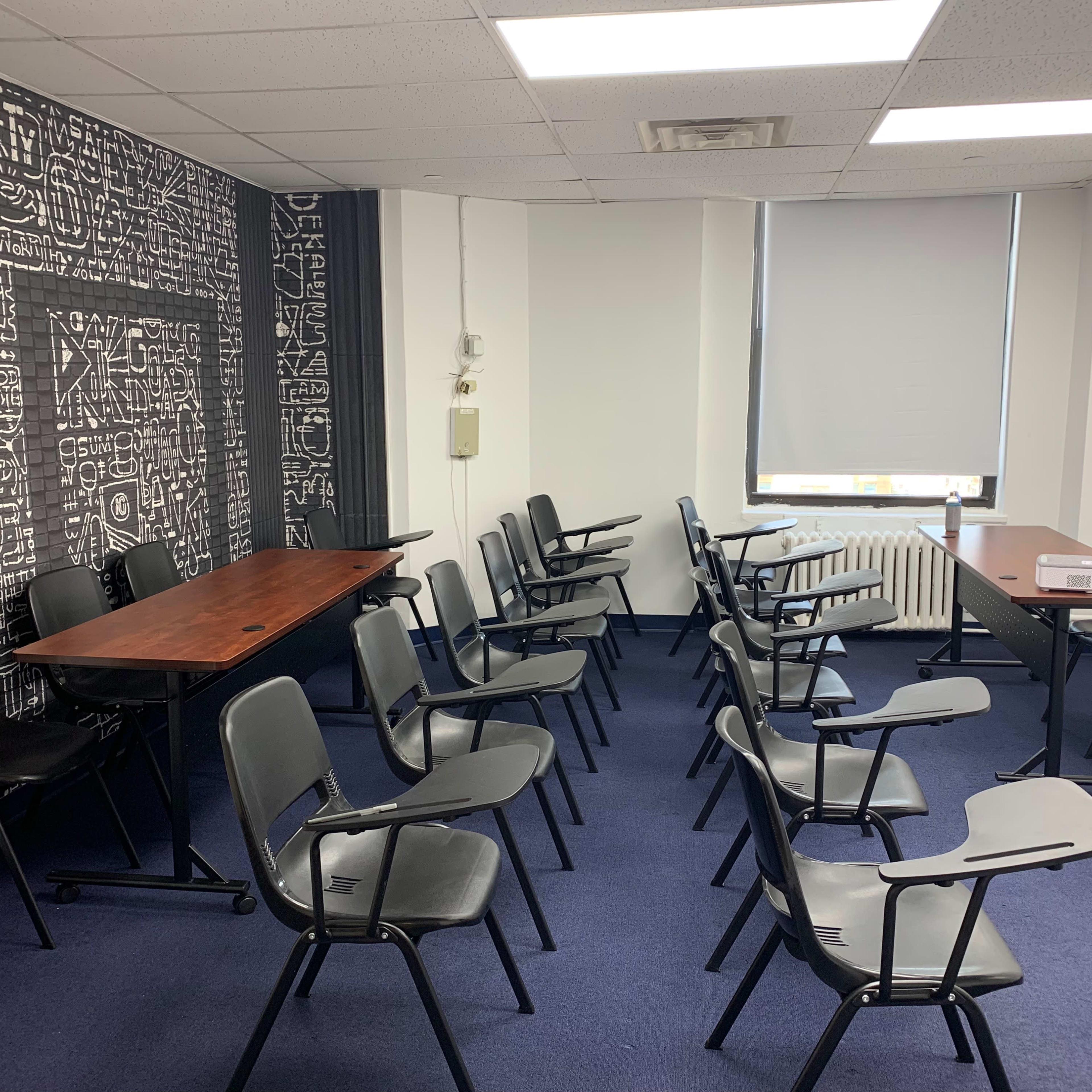 A meeting room with two tables and several black chairs arranged in rows on blue carpeting.