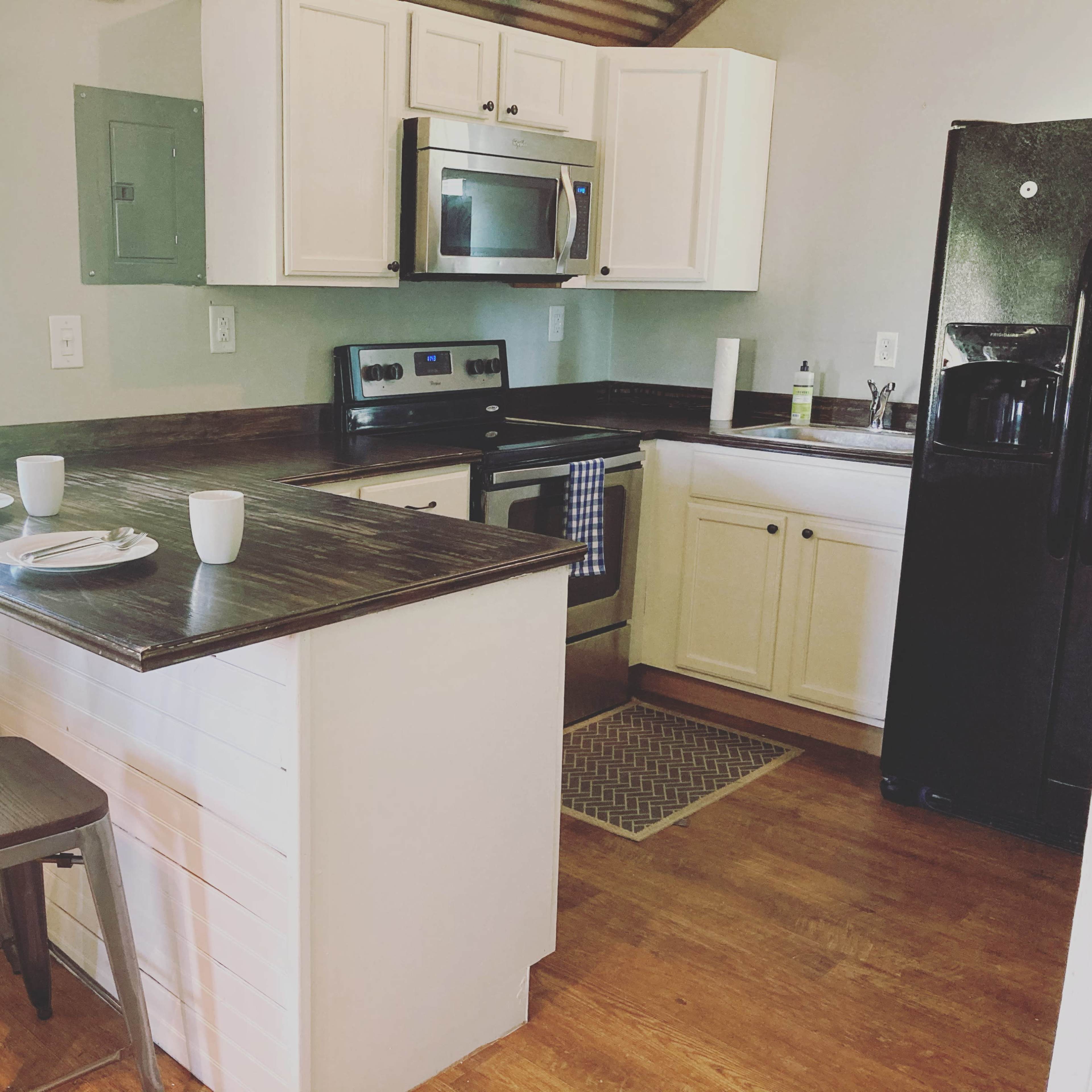 A compact kitchen features white cabinets, stainless steel appliances, and a small bar with two metal stools.