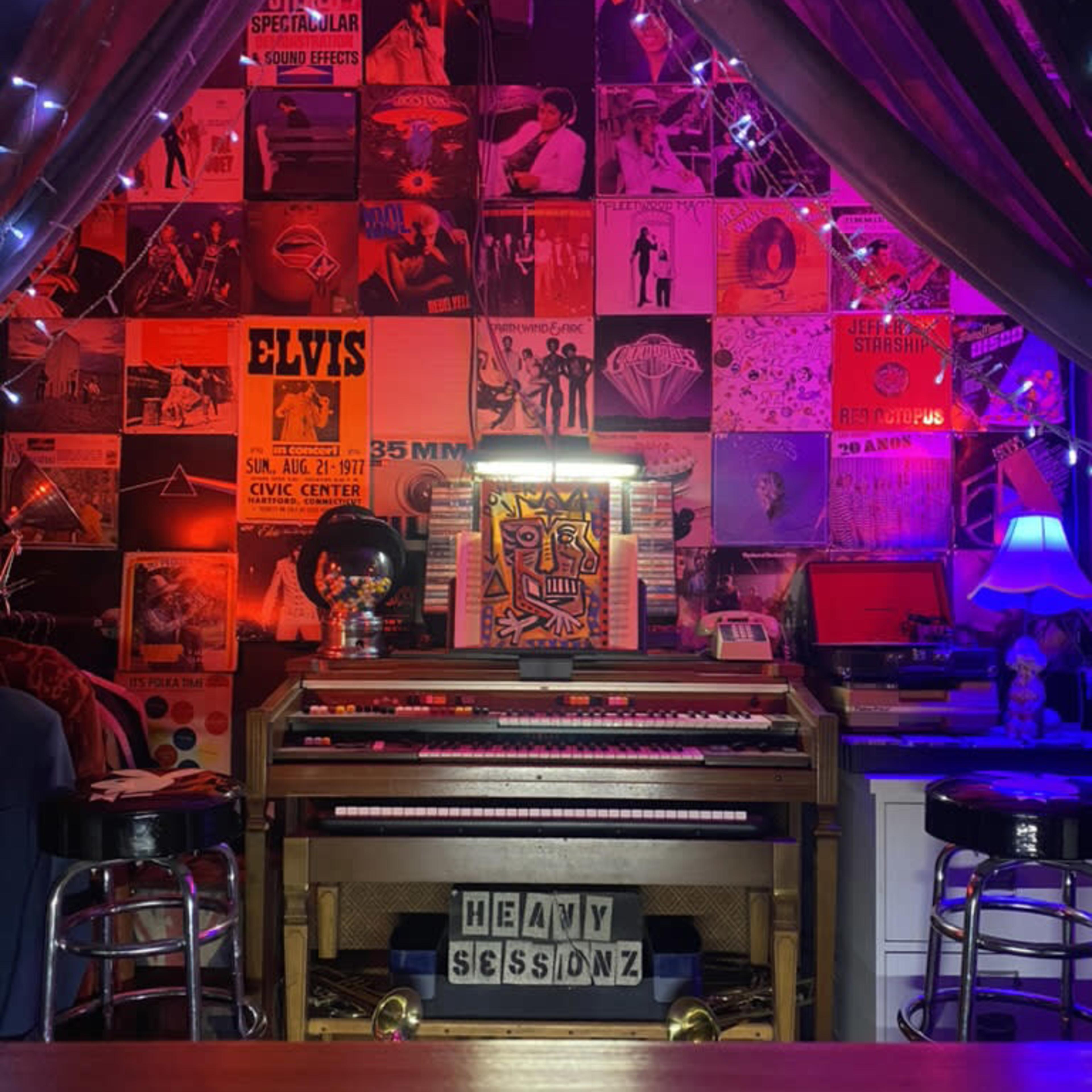 A cozy music room featuring a vintage organ in front of a wall adorned with colorful album covers and ambient lighting.