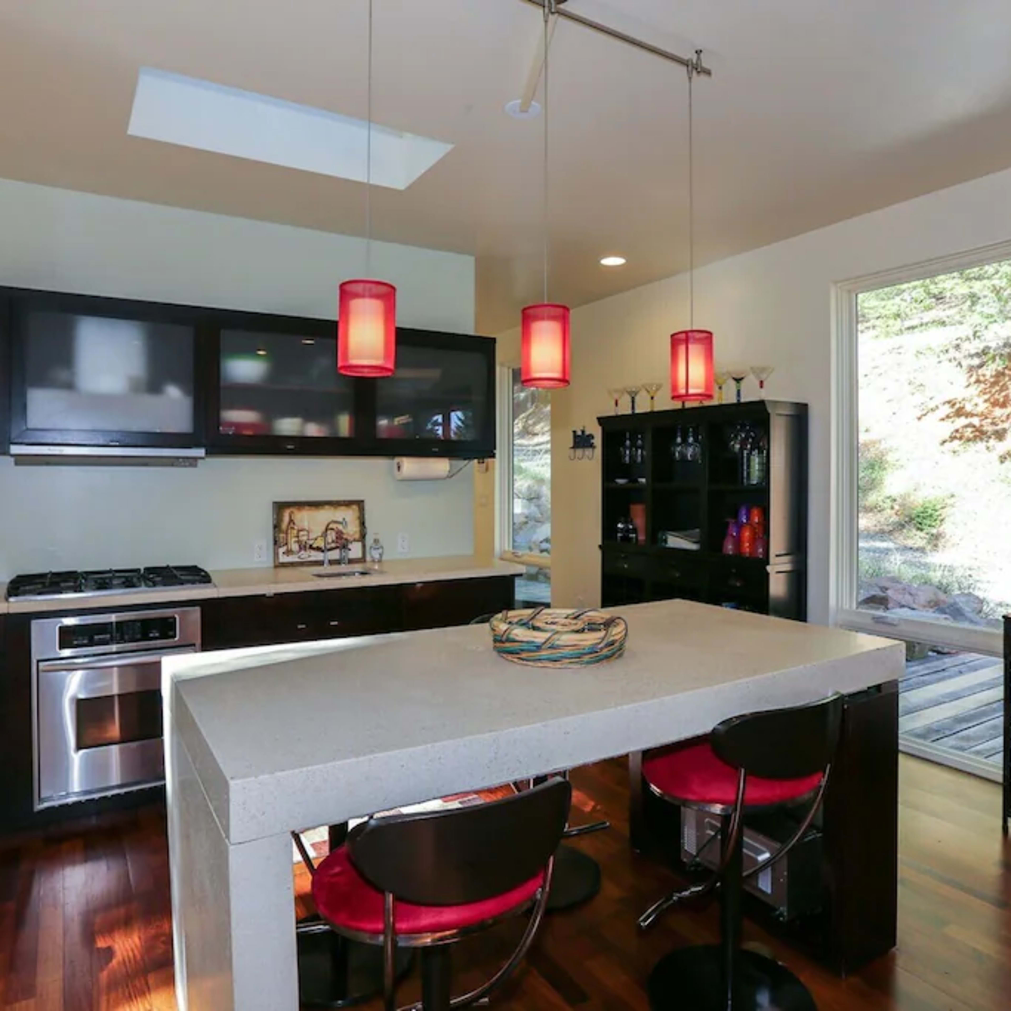 A modern kitchen featuring dark cabinetry, a central island with bar stools, and pendant lights hanging above.