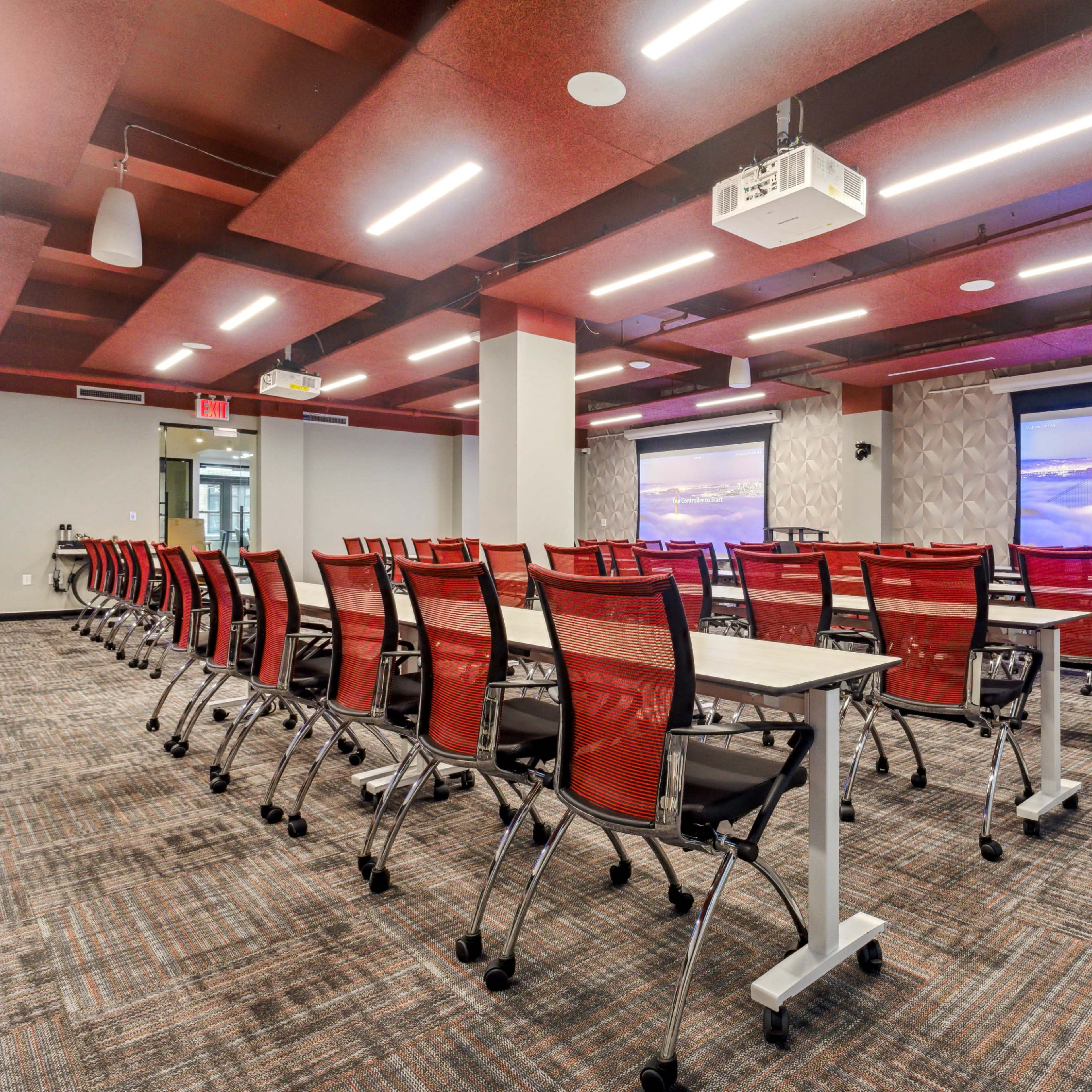 A modern conference room equipped with rows of red chairs facing dual projection screens.