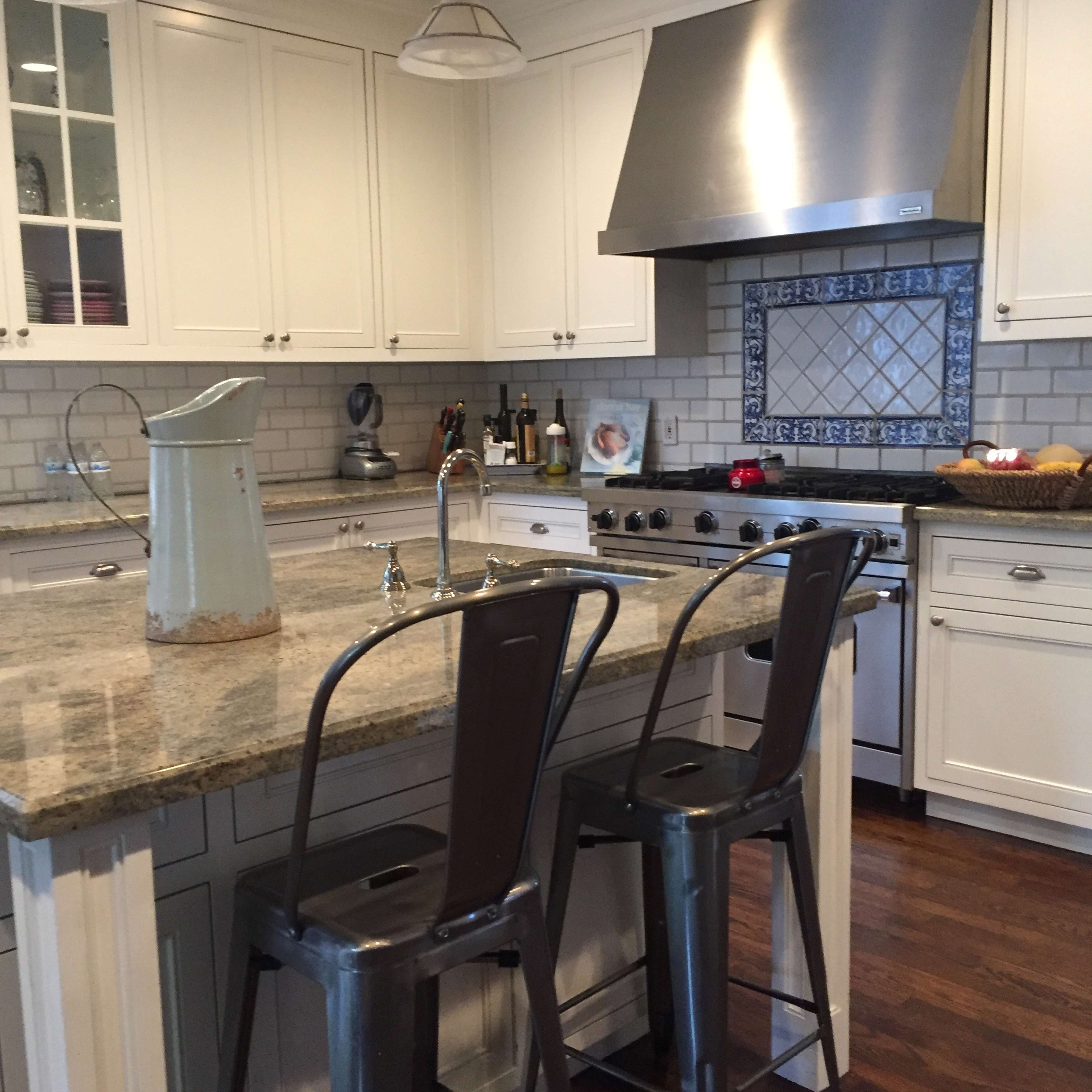 A modern kitchen with white cabinets, a granite countertop, and stainless steel appliances, including a range hood and a stovetop with a backsplash.