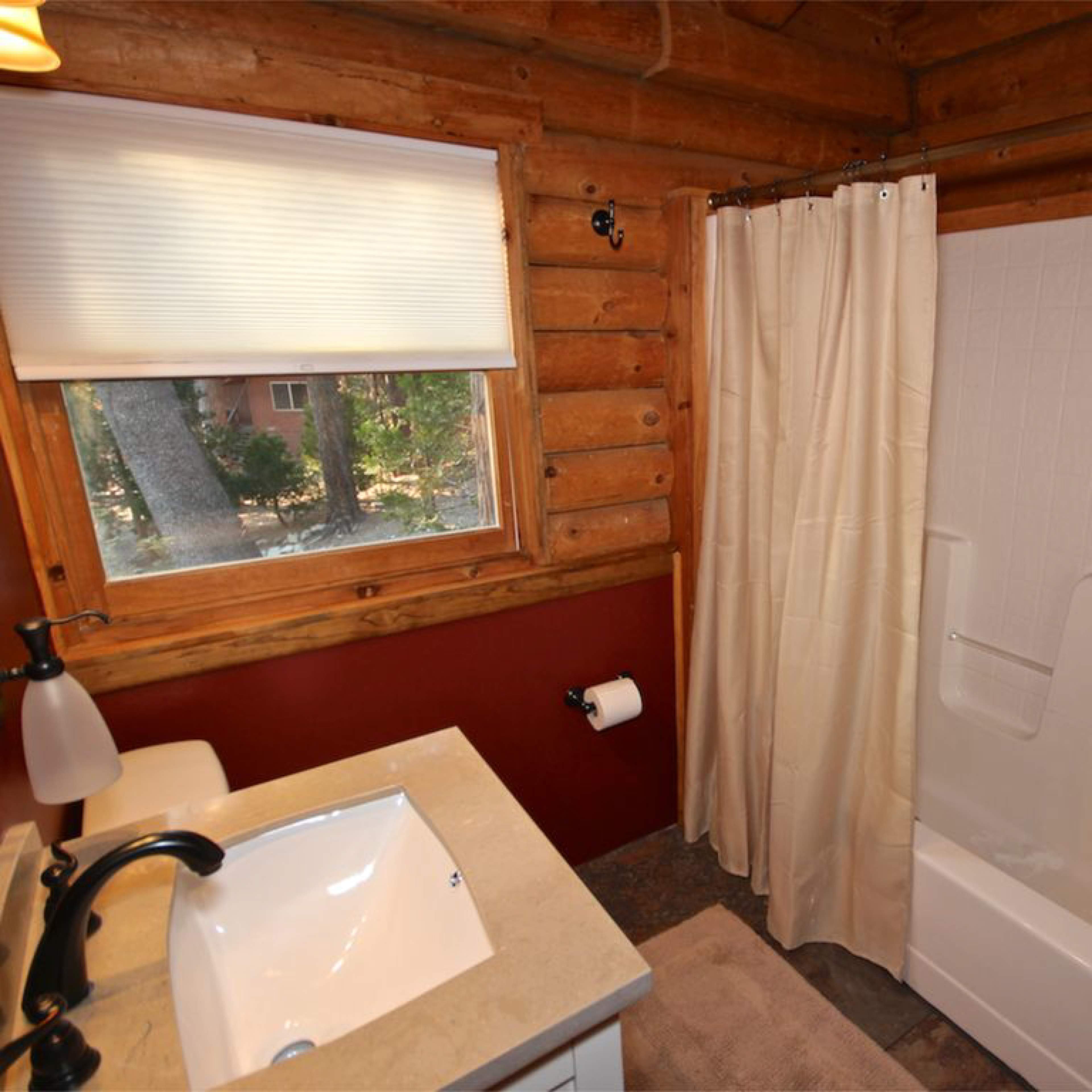 A rustic bathroom featuring a shower-tub combo, a sink with a modern faucet, and wooden walls.