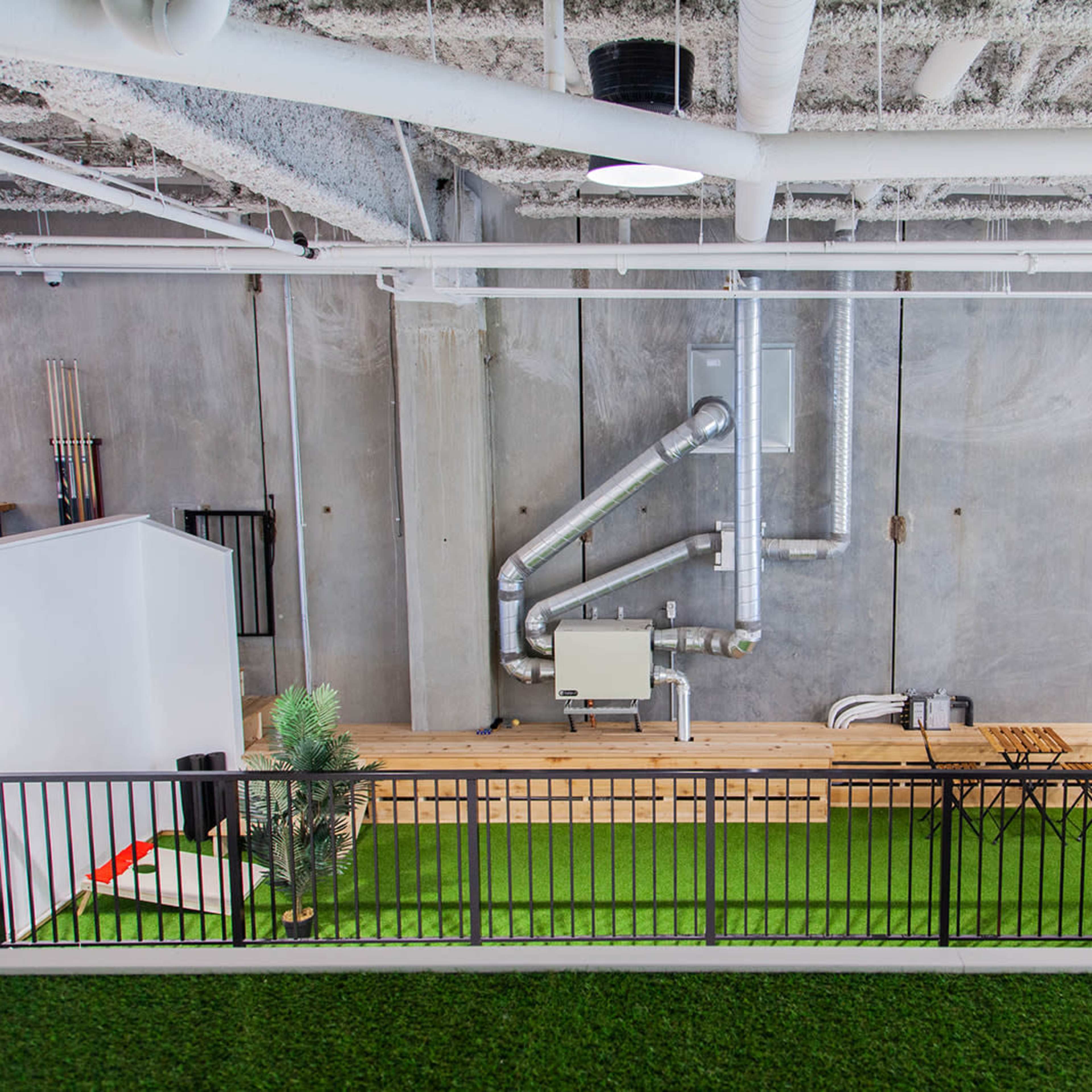 A modern office space featuring a green carpet area with a wooden counter and industrial-style ventilation pipes against a concrete wall adorned with a large bear paw print.