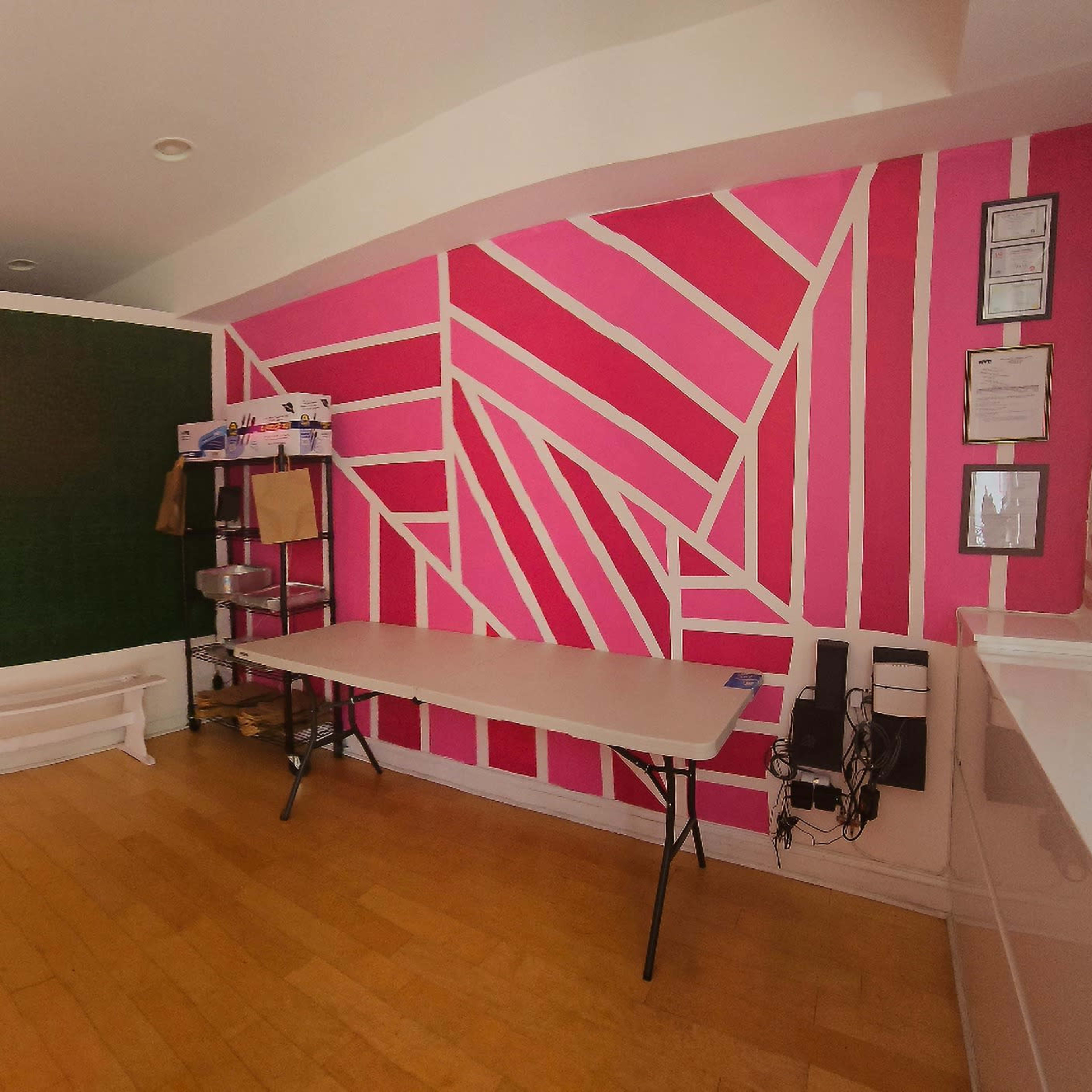 A brightly decorated interior space with pink and white geometric patterns on the walls and a green section, along with a table and chairs.